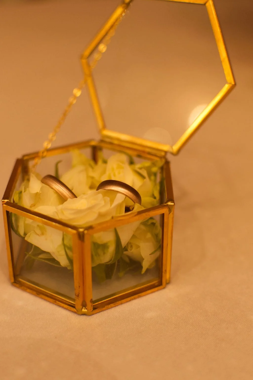 Zwei Eheringe liegen auf weißen Blüten in einer goldenen Glasbox, die geöffnet ist.