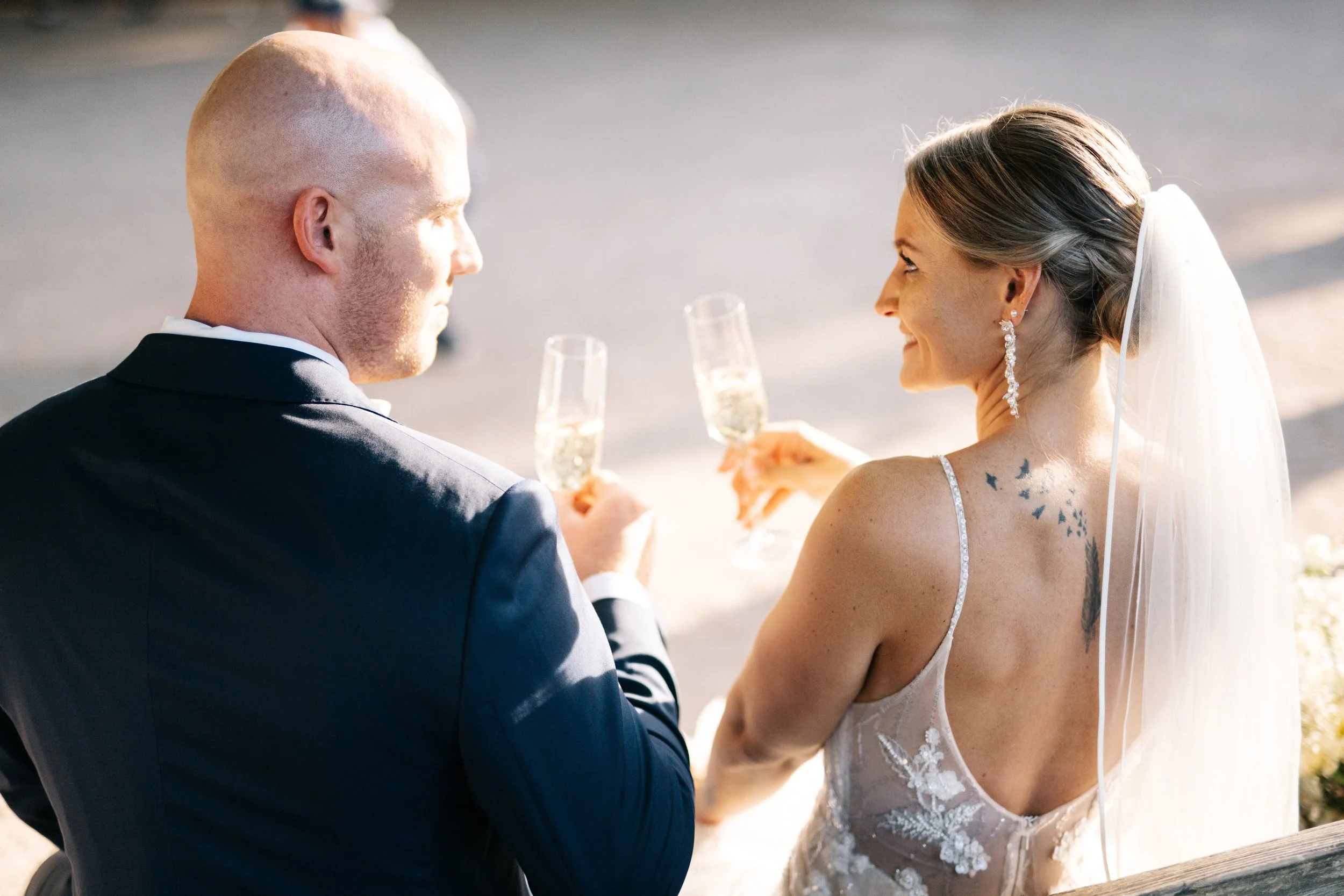 Braut und Bräutigam bei ihrer Hochzeit, sie stoßen mit Champagner an, im Freien bei Sonnenuntergang.