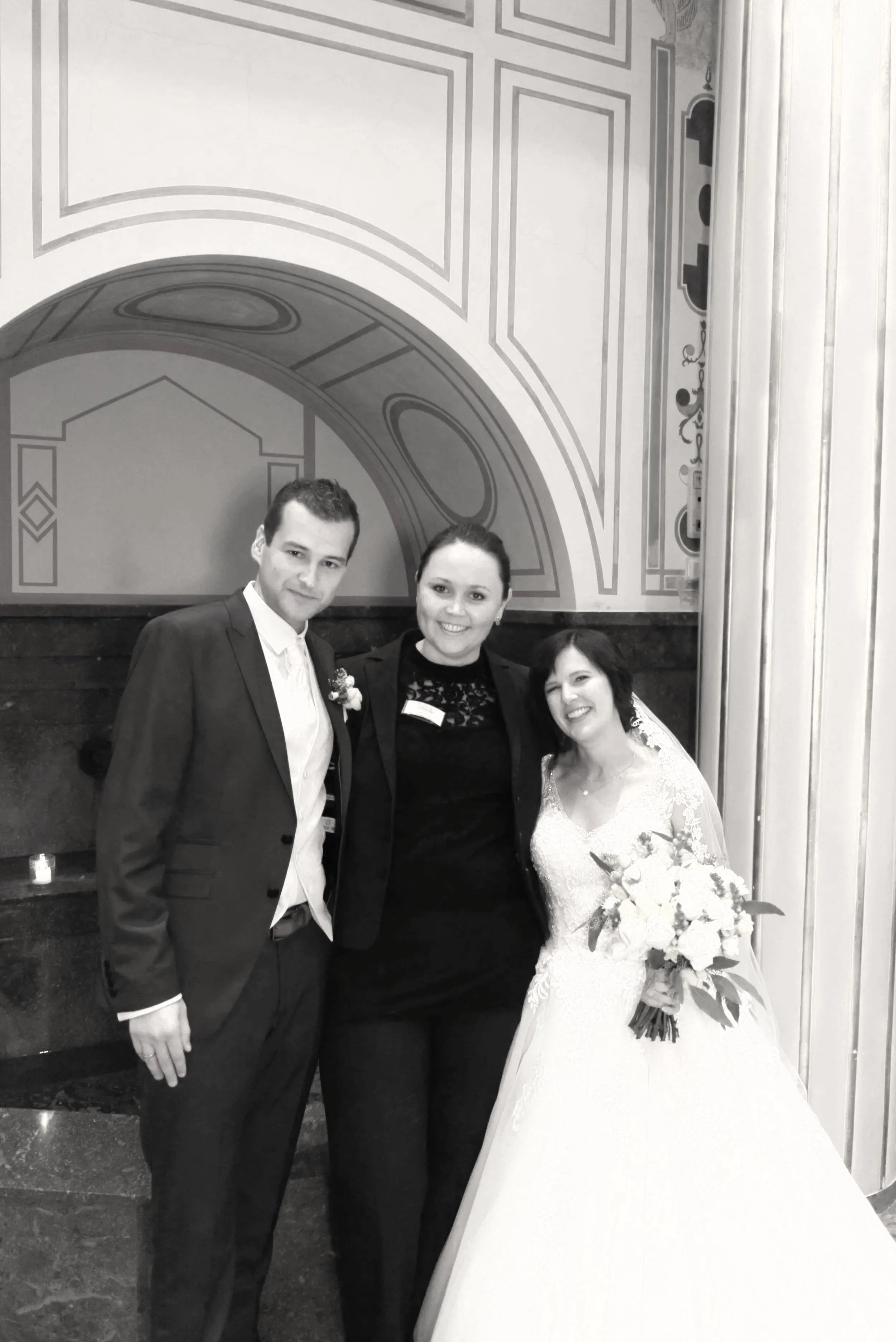 Drei Personen, ein Mann, eine Frau und eine Braut, posieren in einem festlichen Rahmen, wahrscheinlich bei einer Hochzeit.