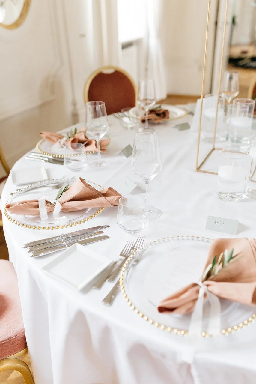 Elegant gedeckter Esstisch mit Tellern, Besteck, Weingläsern, Kerzen, Stoffservietten und Platzkarten im schön dekorierten Raum.