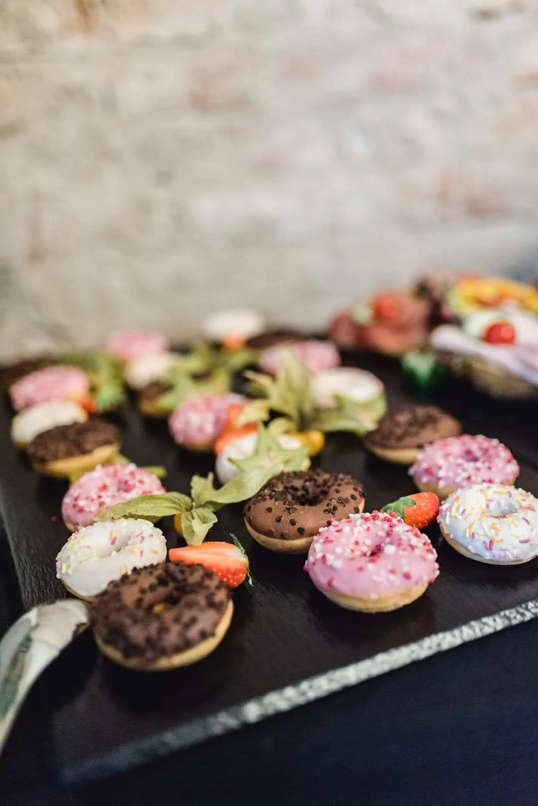 Verschiedene bunte Donuts mit Schokolade, Frucht und Zuckerdekoration auf einem schwarzen Serviertablett