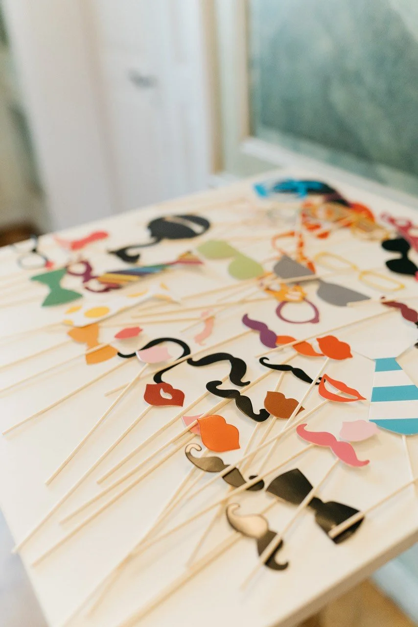 Verschiedene bunte Partydekorationen auf einem Tisch, darunter Papp-Schnurrbärte, Lippen und Hüte, vermutlich für eine Party oder Feier.