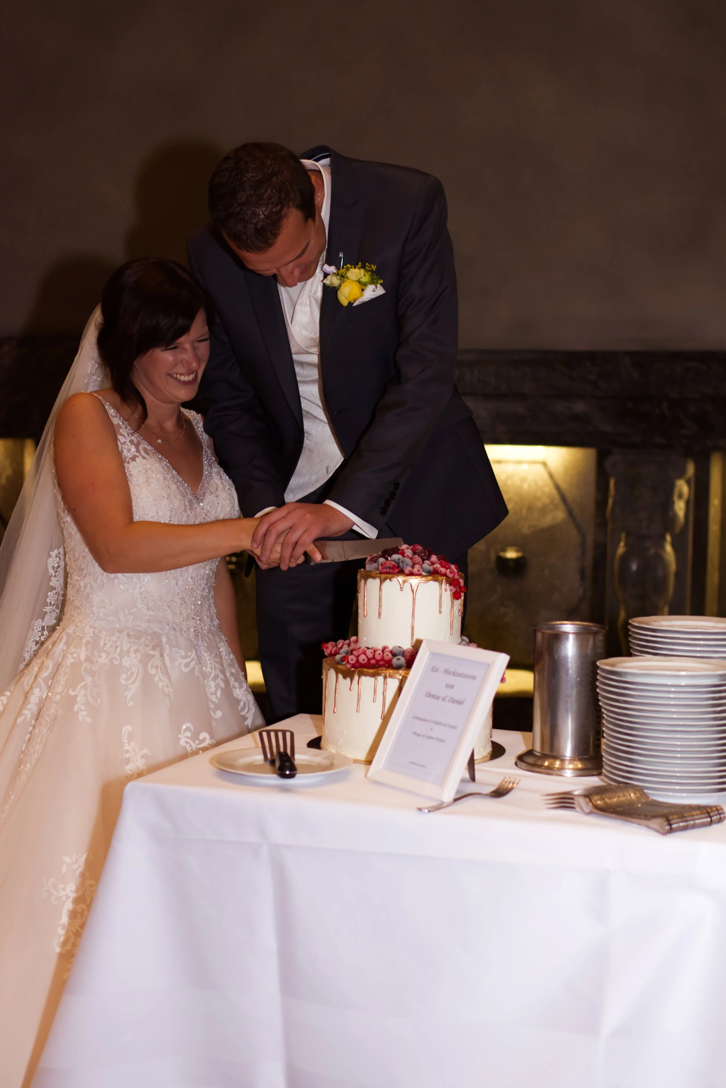 Ein Brautpaar schneidet eine Hochzeitstorte bei ihrer Feier, die Torte ist mit Beeren dekoriert.