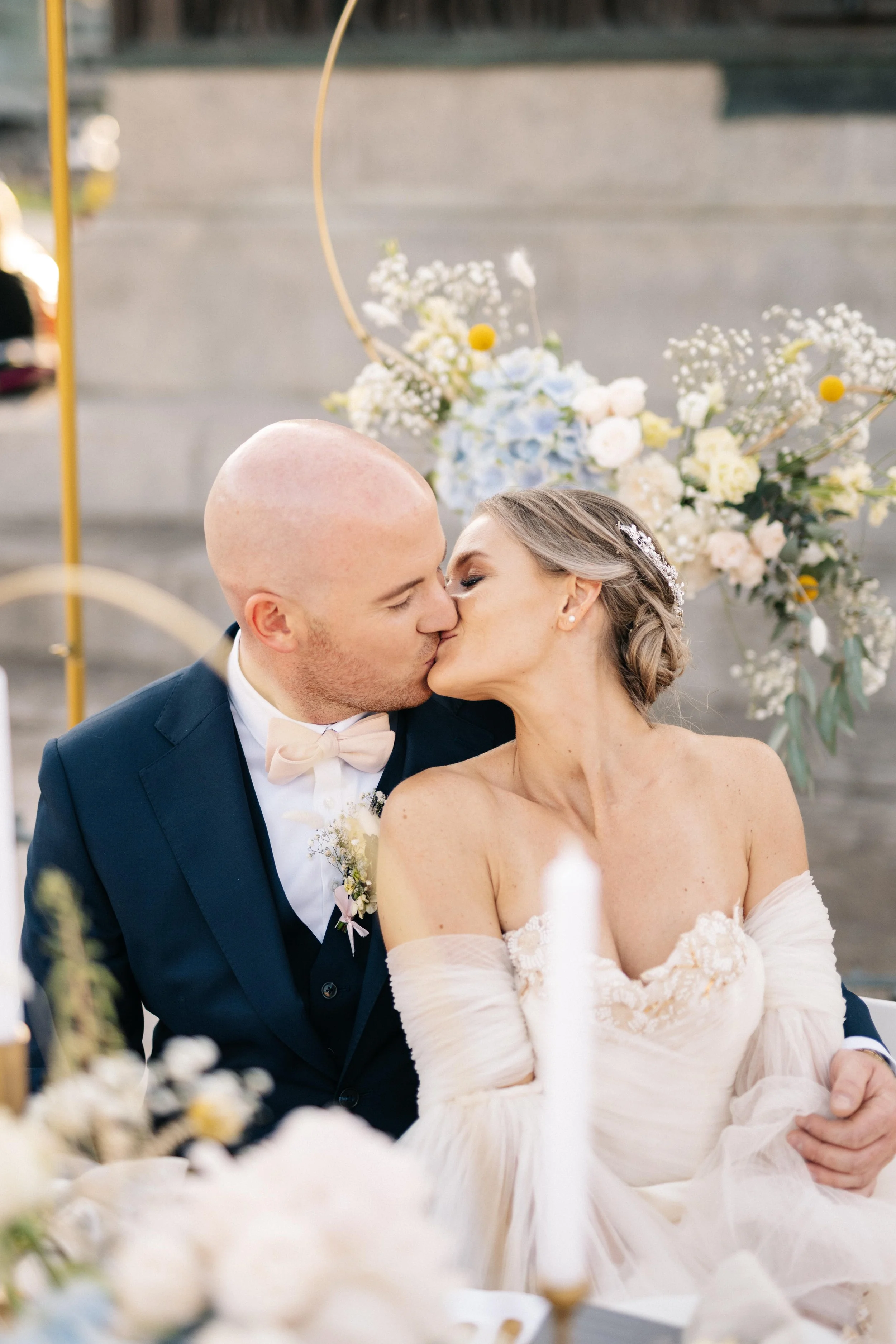 Ein frisch verheiratetes Paar küsst sich bei ihrer Hochzeit, im Hintergrund eine Blumen