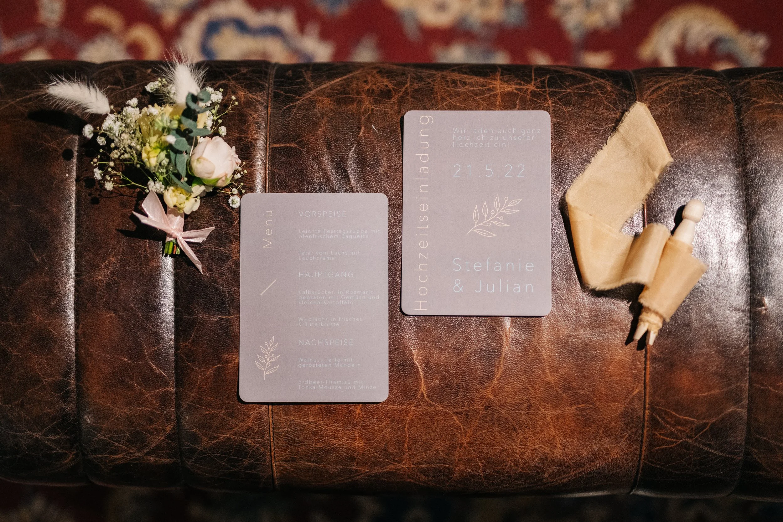 Hochzeitseinladung auf braunem Lederhocker mit Blumen, Menükarte und Holz-Accessoires.