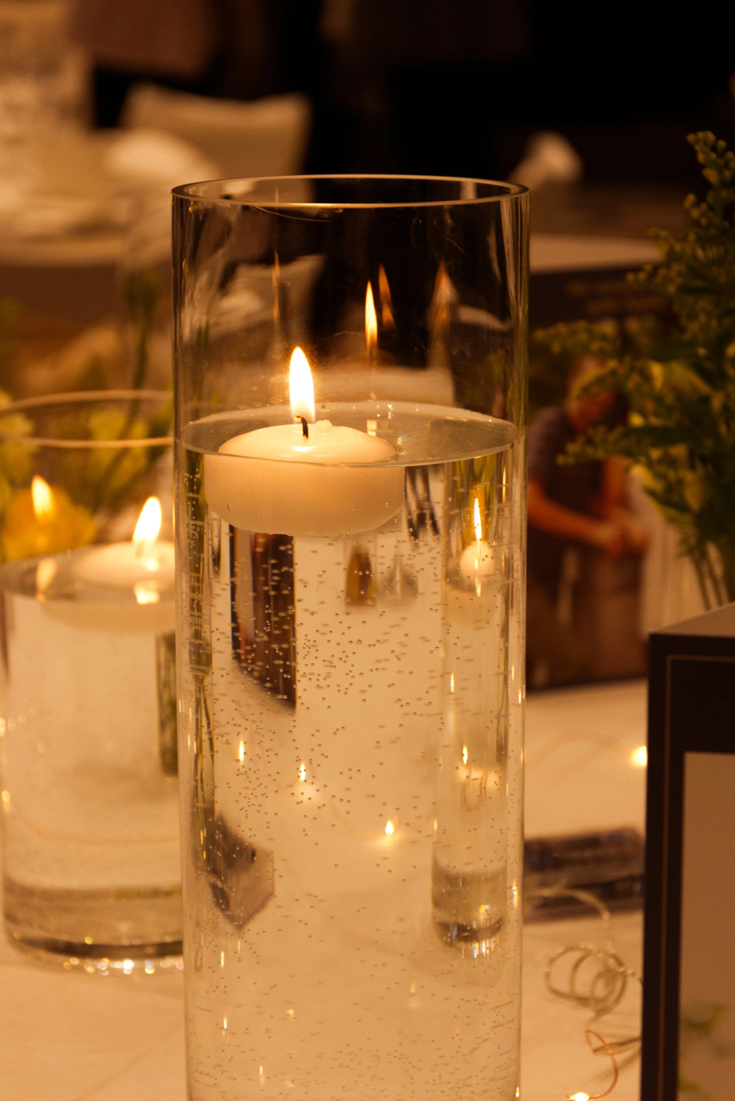 Kerzen in einem hohen Glasbehälter mit Wasser und Luftblasen, warmes Licht auf einer festlich gedeckten Tafel.