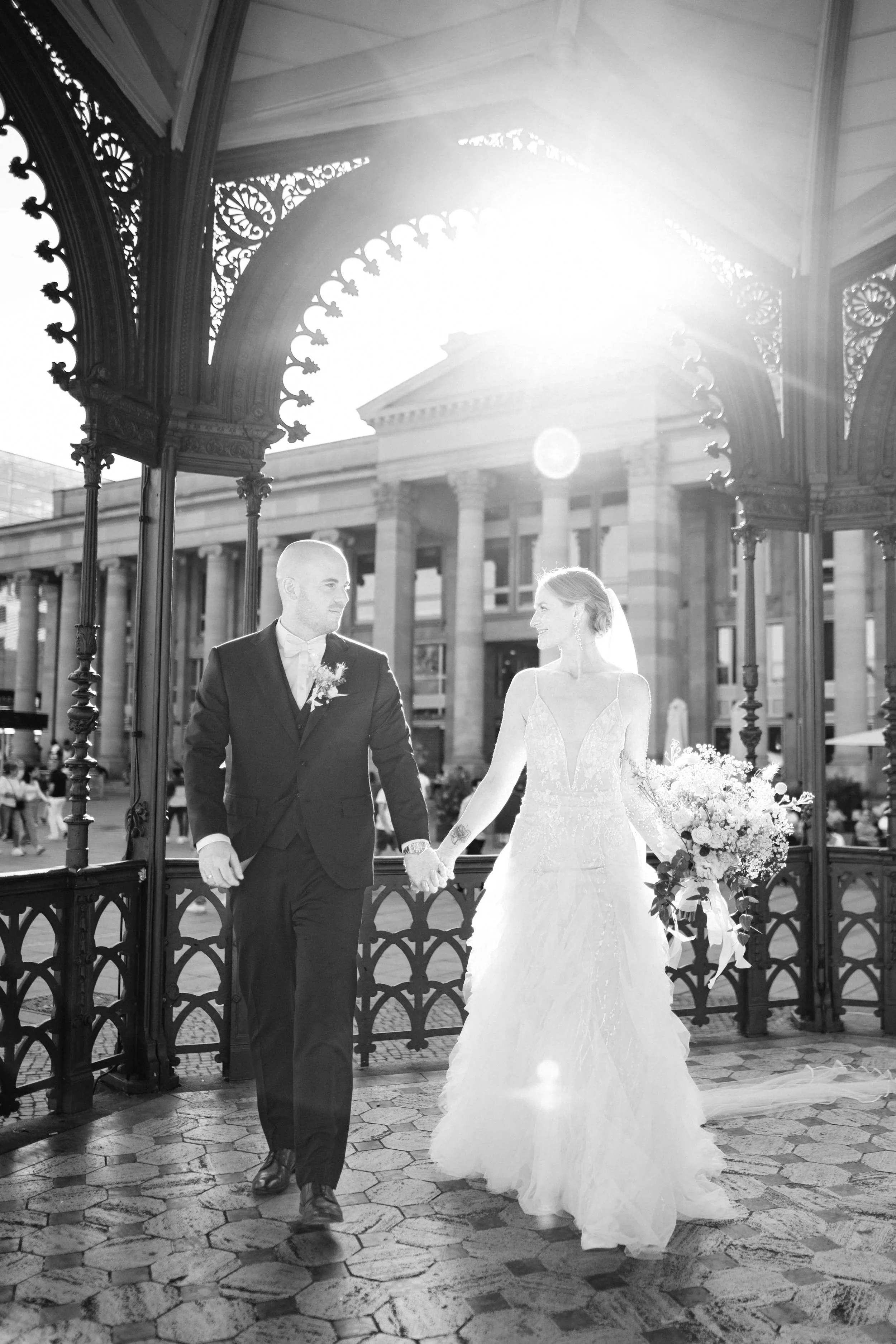 Ein Brautpaar in formeller Kleidung, die Hand in Hand gehen, draußen bei Sonnenuntergang, im schwarzen und weißen Foto, am Felsen.
