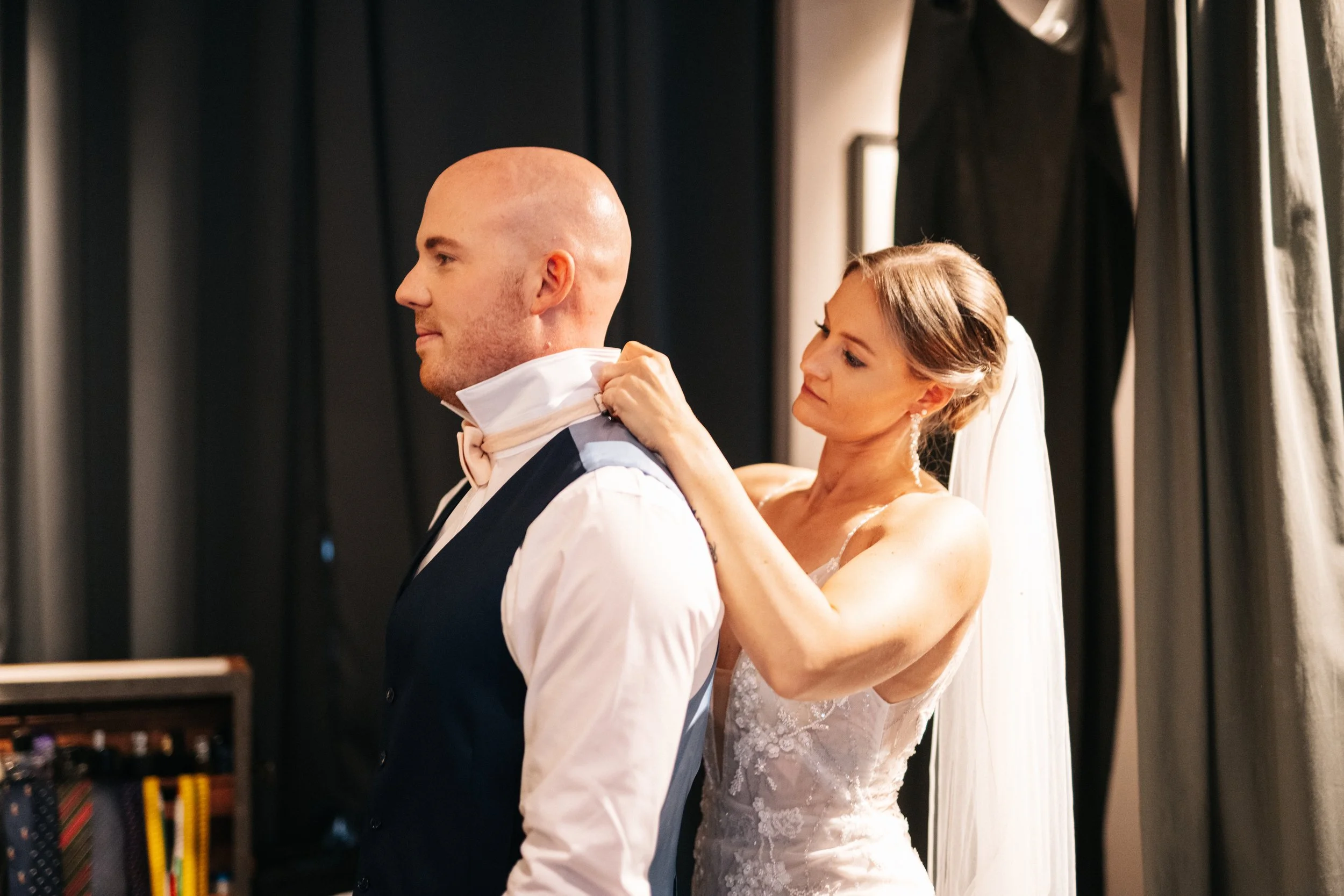 Braut hilft Bräutigam, seine Jacke beim Hochzeitskleid anzulegen.