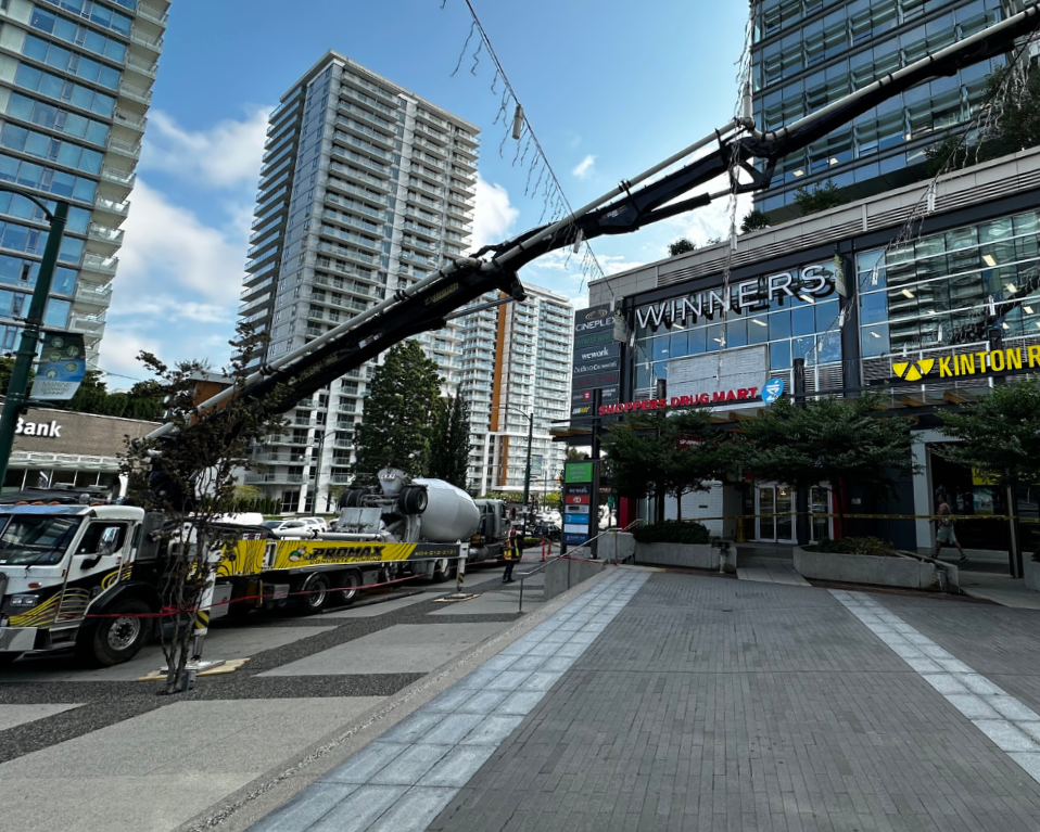 A street scene with high-rise buildings, a fallen utility pole, and a crew truck repairing the power lines. There is a shopping center called Winners and a drugmart, with a few pedestrians nearby.