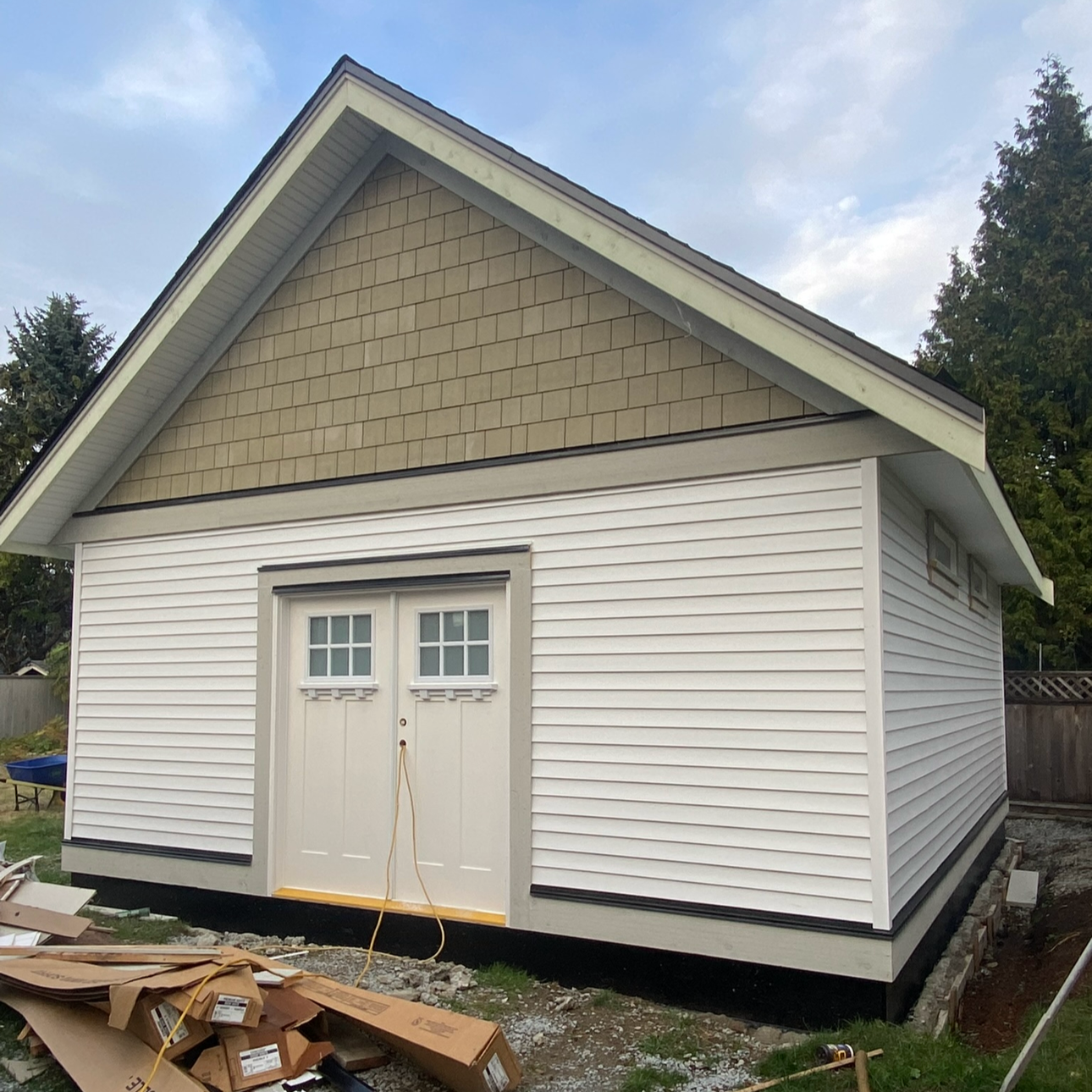 Newly constructed small building with white siding, double doors, and a gable roof, surrounded by construction materials.