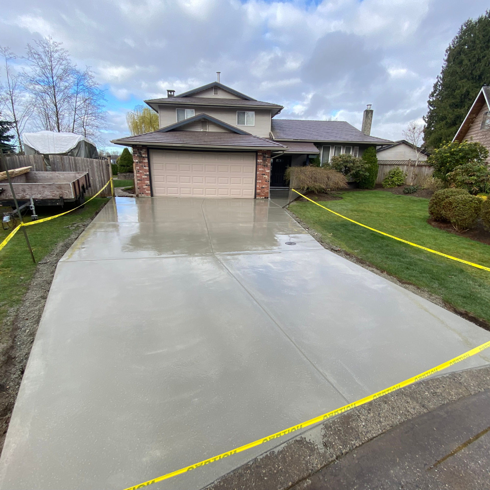 Newly poured concrete driveway in front of a house, surrounded by yellow caution tape.