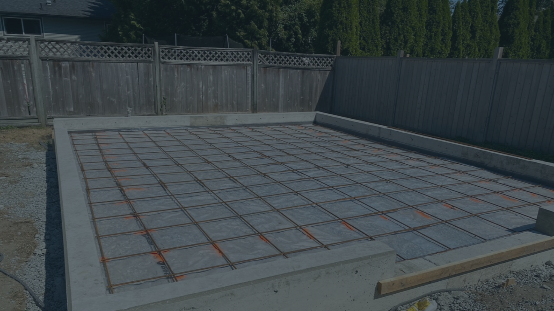 Construction site with concrete slab and metal rebar grid for foundation pouring, surrounded by fencing.