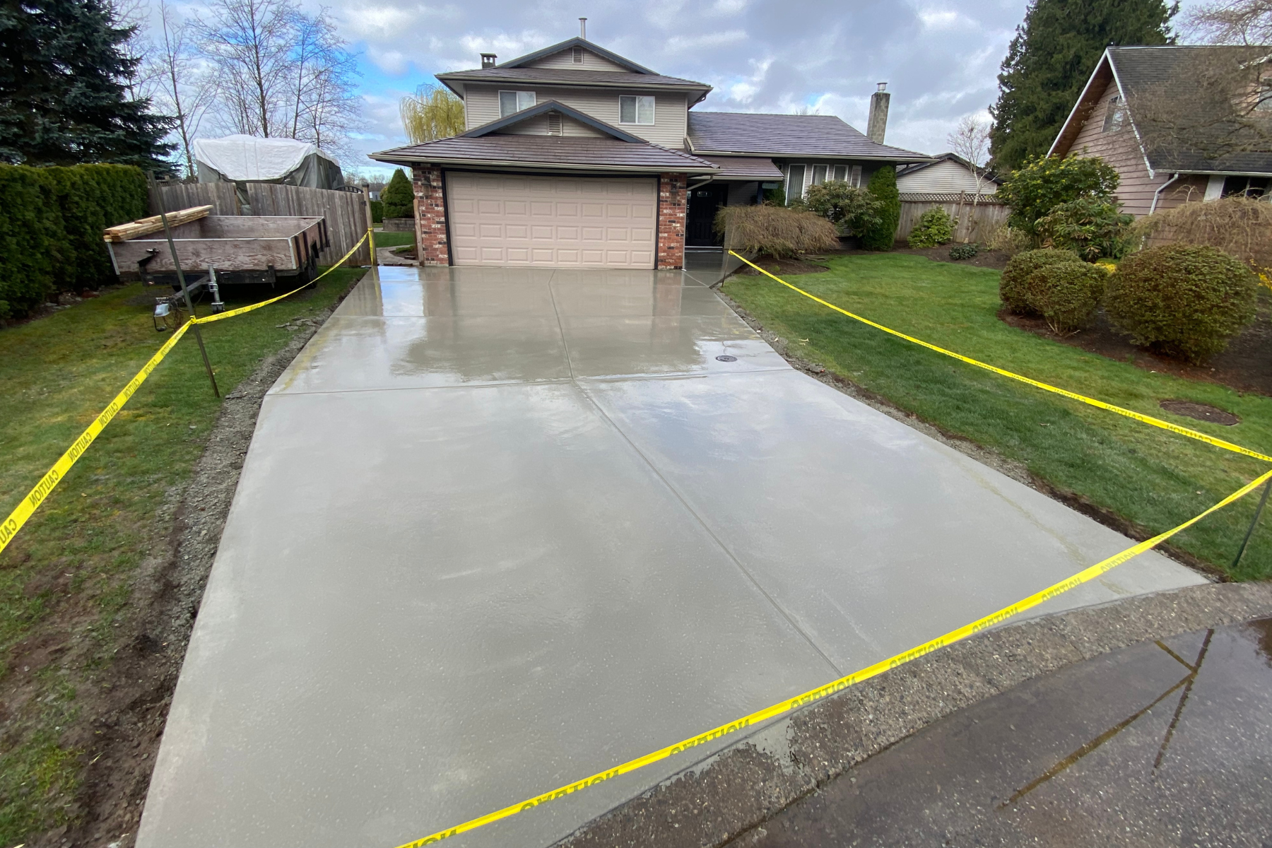Newly poured concrete driveway in front of house, surrounded by yellow caution tape.
