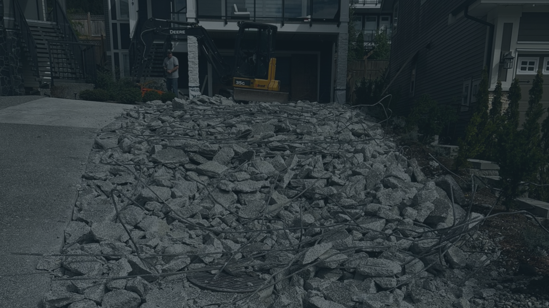 Construction site with broken concrete and rebar, with a small excavator and two workers in the background