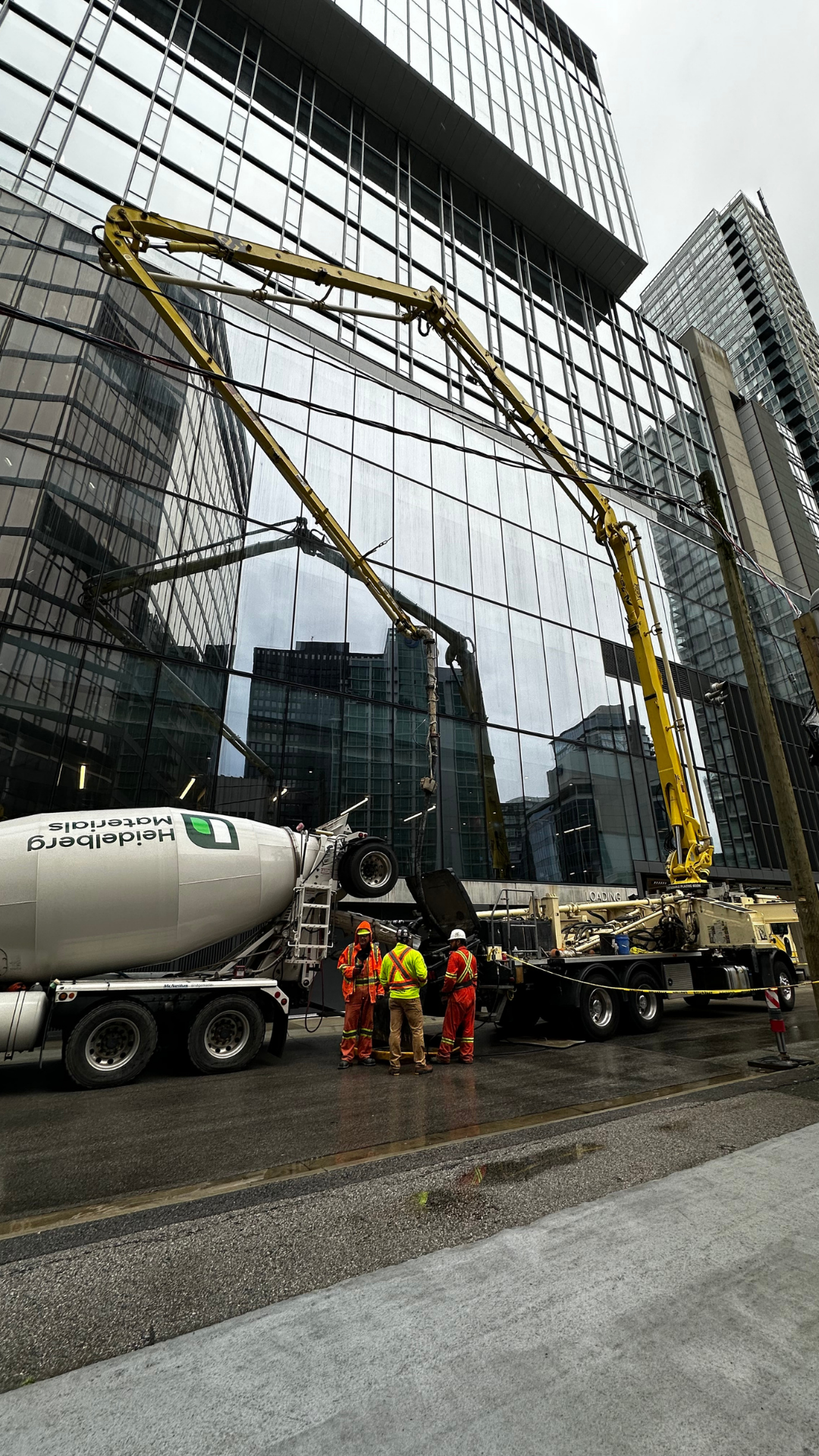 Construction workers in safety gear working on a building construction site with cement mixer truck and large concrete pump.