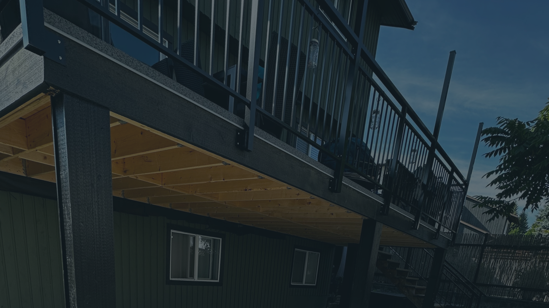 Image of a house with a new wooden deck and black metal railing.