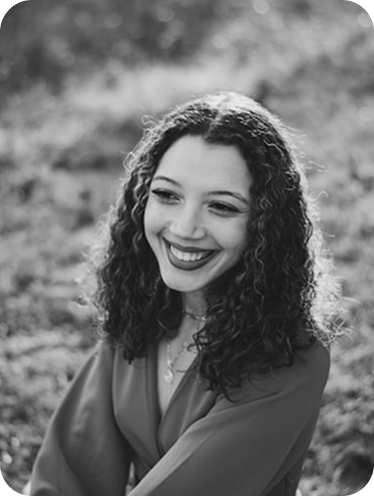 A smiling woman with curly hair outdoors in black and white.