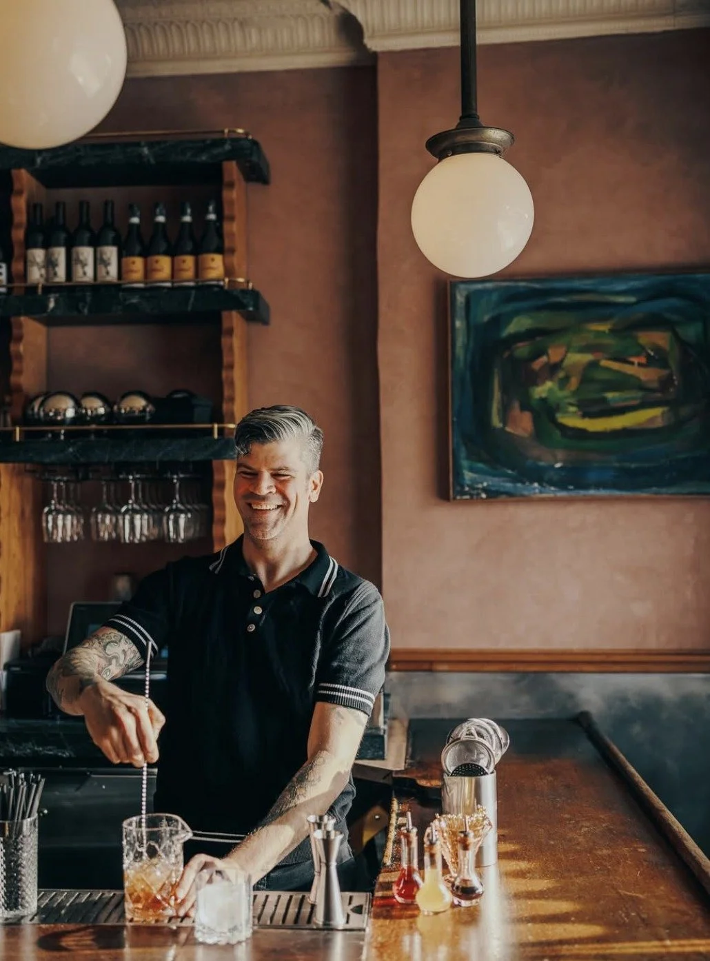 Scott behind the bar, stirring a cocktail in a mixing glass.
