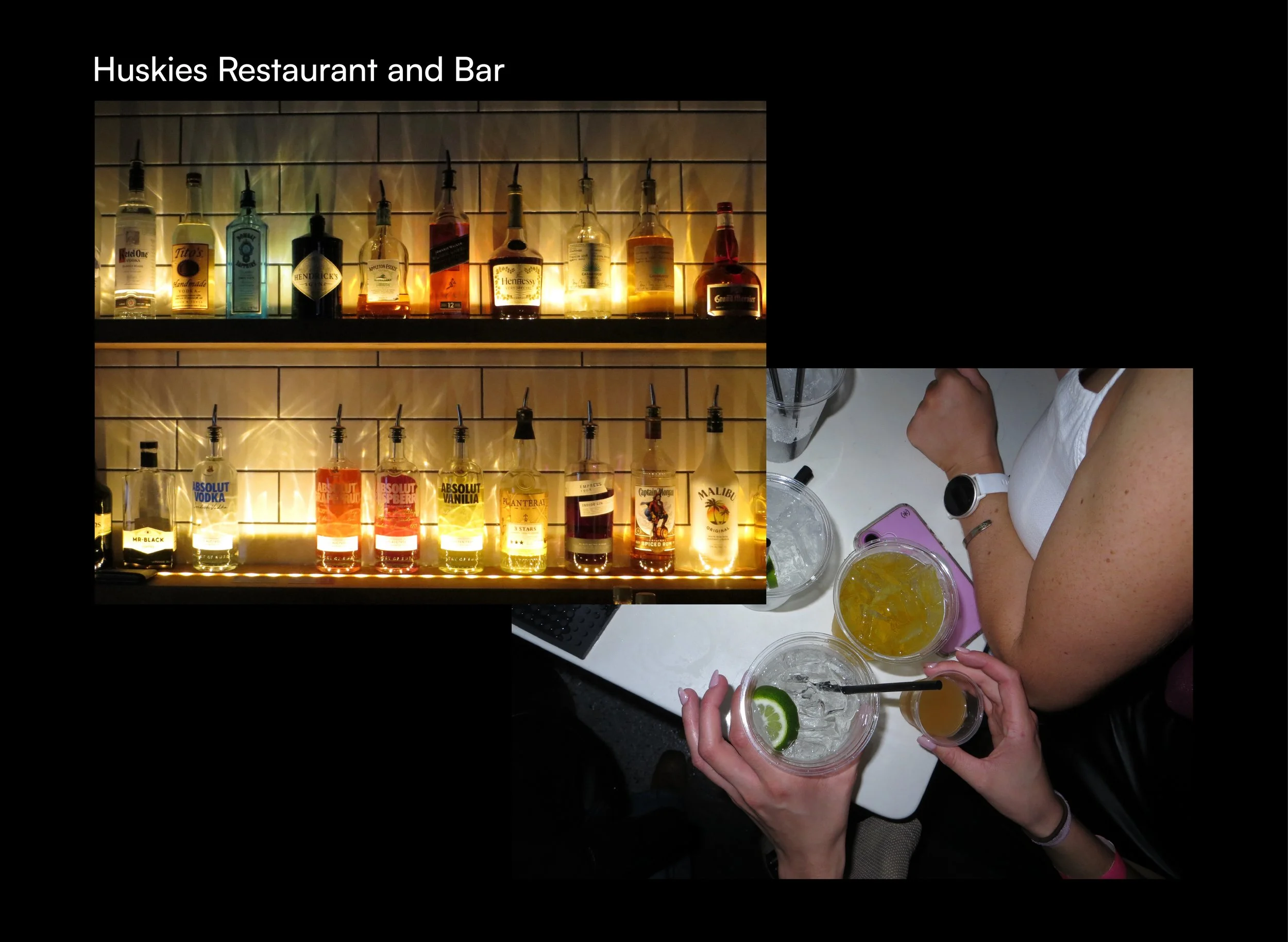 A bar display with various bottles of alcohol behind the counter and two people holding cocktails garnished with lime slices and ice on a white table.