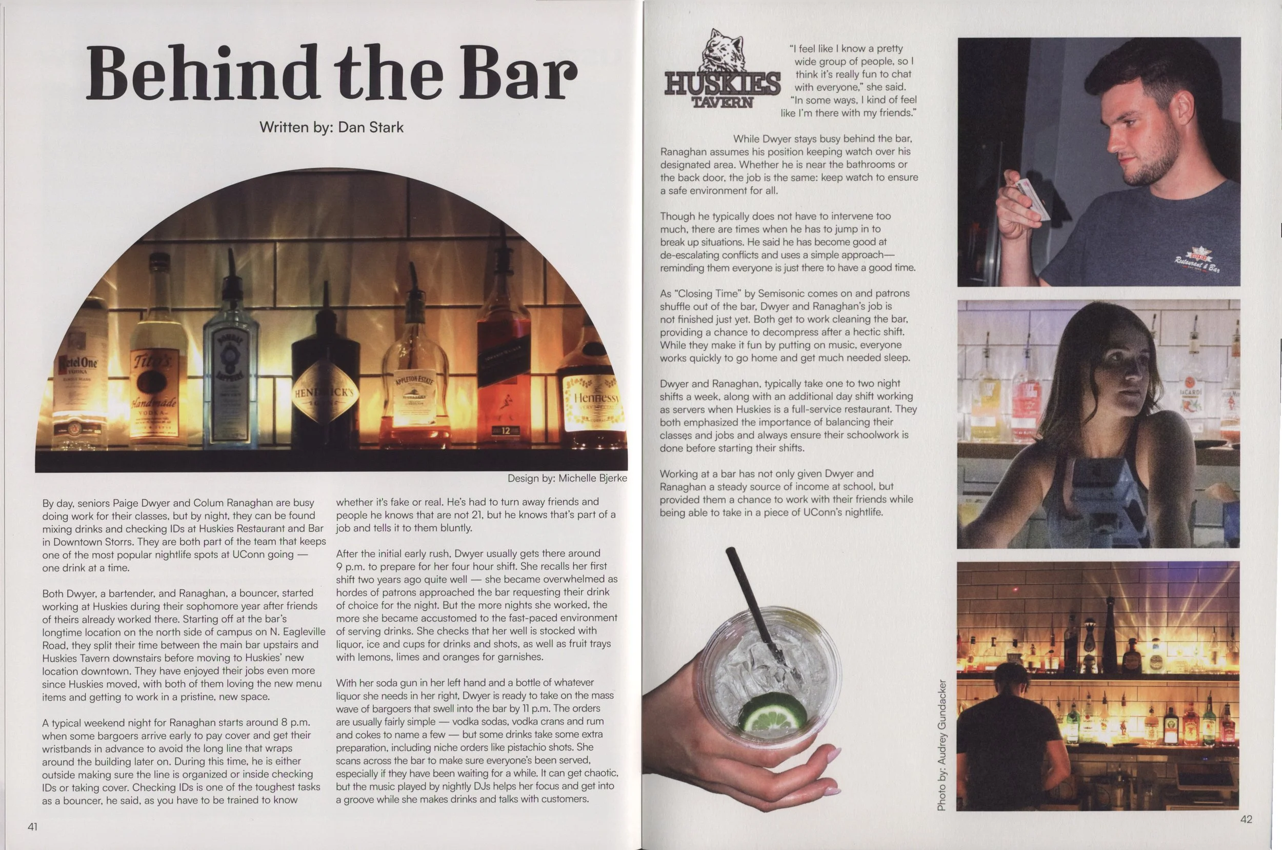 Page spread from a magazine or booklet featuring a headline titled "Behind the Bar" with a subheading stating "Written by: Dan Stark." The left side displays a photo of various liquor bottles on a bar shelf, with some bottles visible, including Tullamore Dew, Hendrick's, and Appleton Estate. The right side includes text about bartenders Paige Dwyer and Colum Ragnahan, along with a photo of a young man with dark hair, a beard, and wearing a dark-colored shirt, holding a shot glass, and a photo of a woman with long dark hair and bangs, sitting at the bar. Another photo shows the bar area illuminated with pendant lights and shelves stocked with liquor bottles, and there is a drink with a lime wedge and a straw at the bottom center of the page.