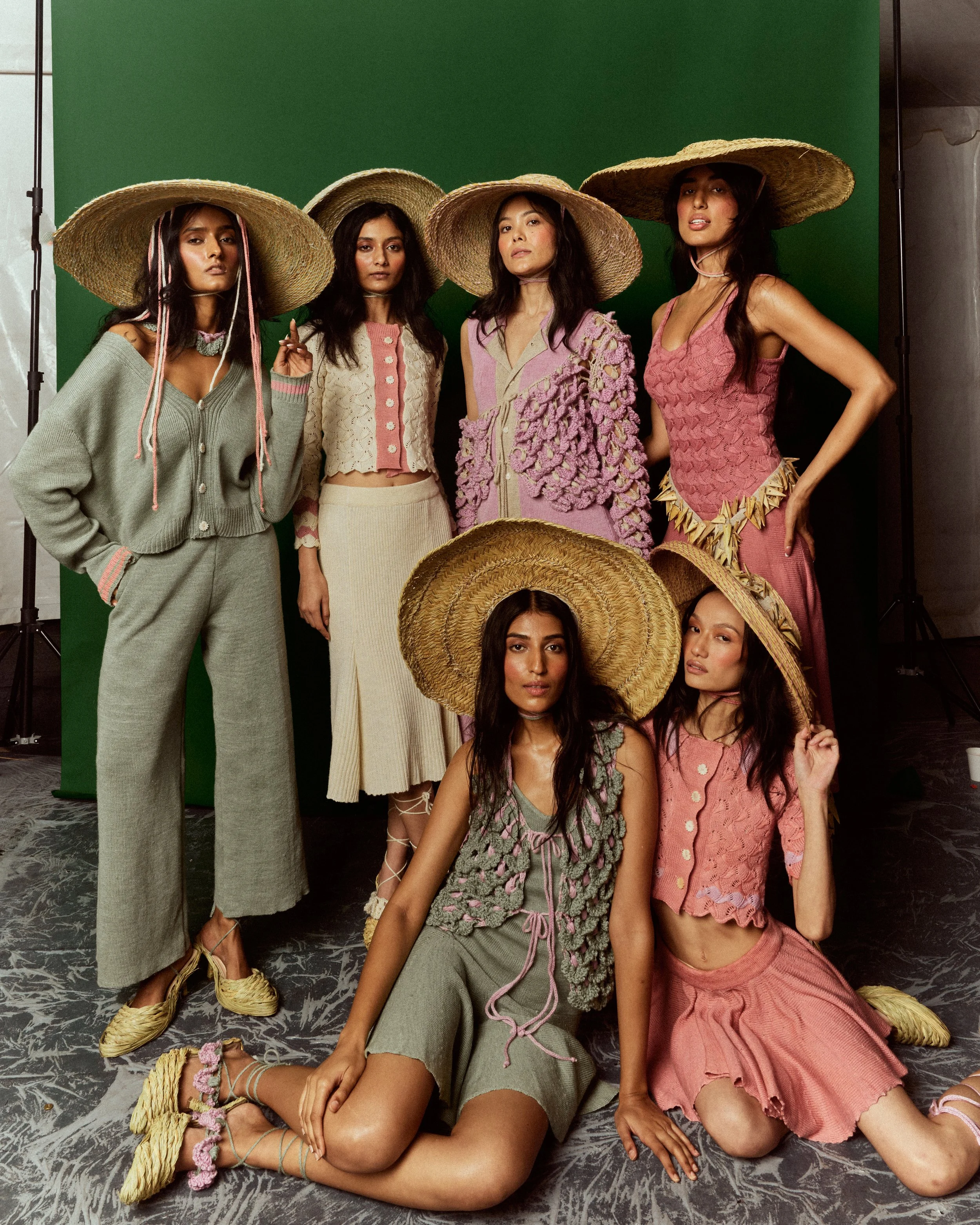 Four women wearing large straw hats and fashionable clothing pose in front of a green screen.
