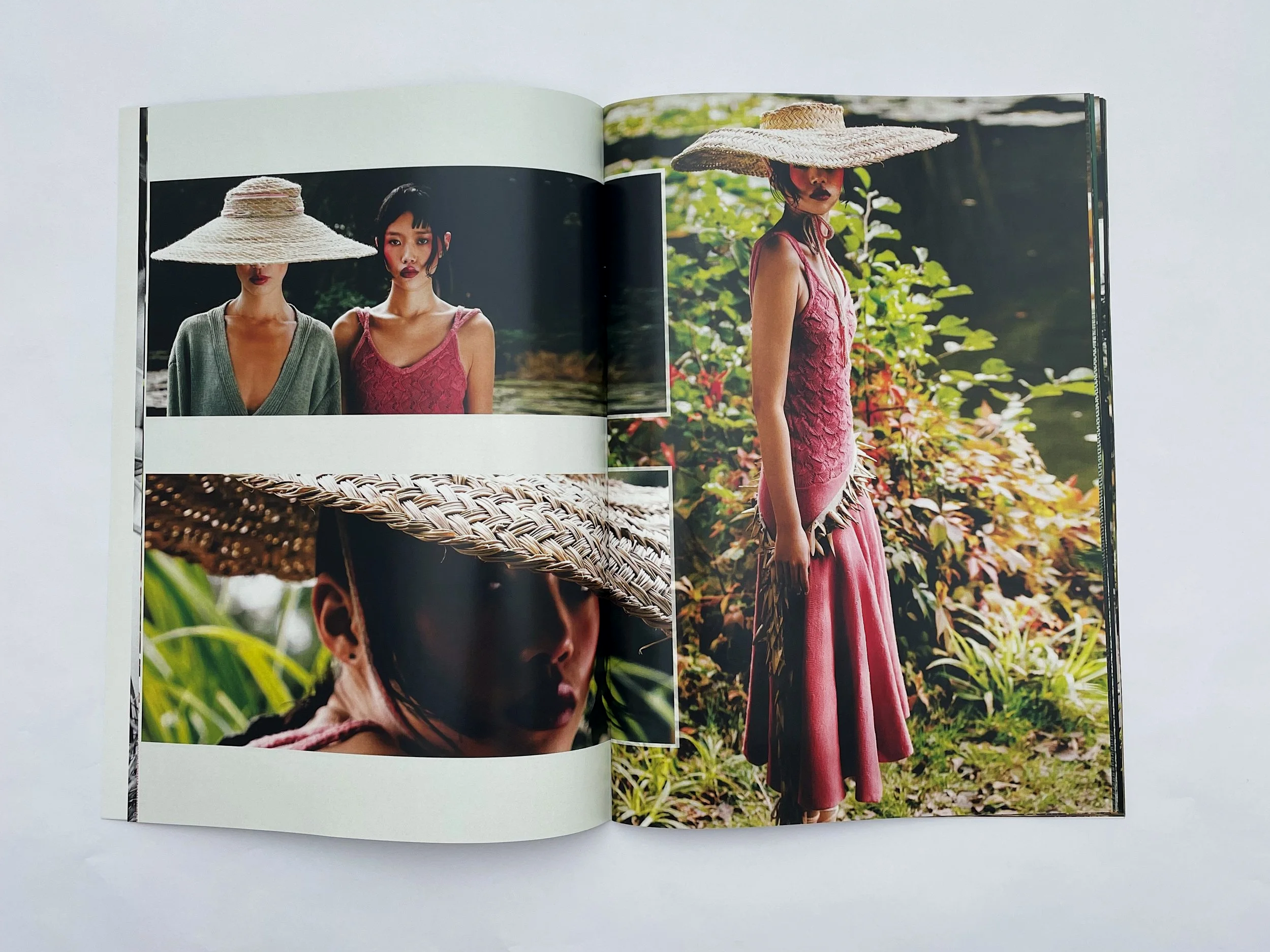 Open magazine depicting models wearing straw hats outdoors surrounded by greenery.