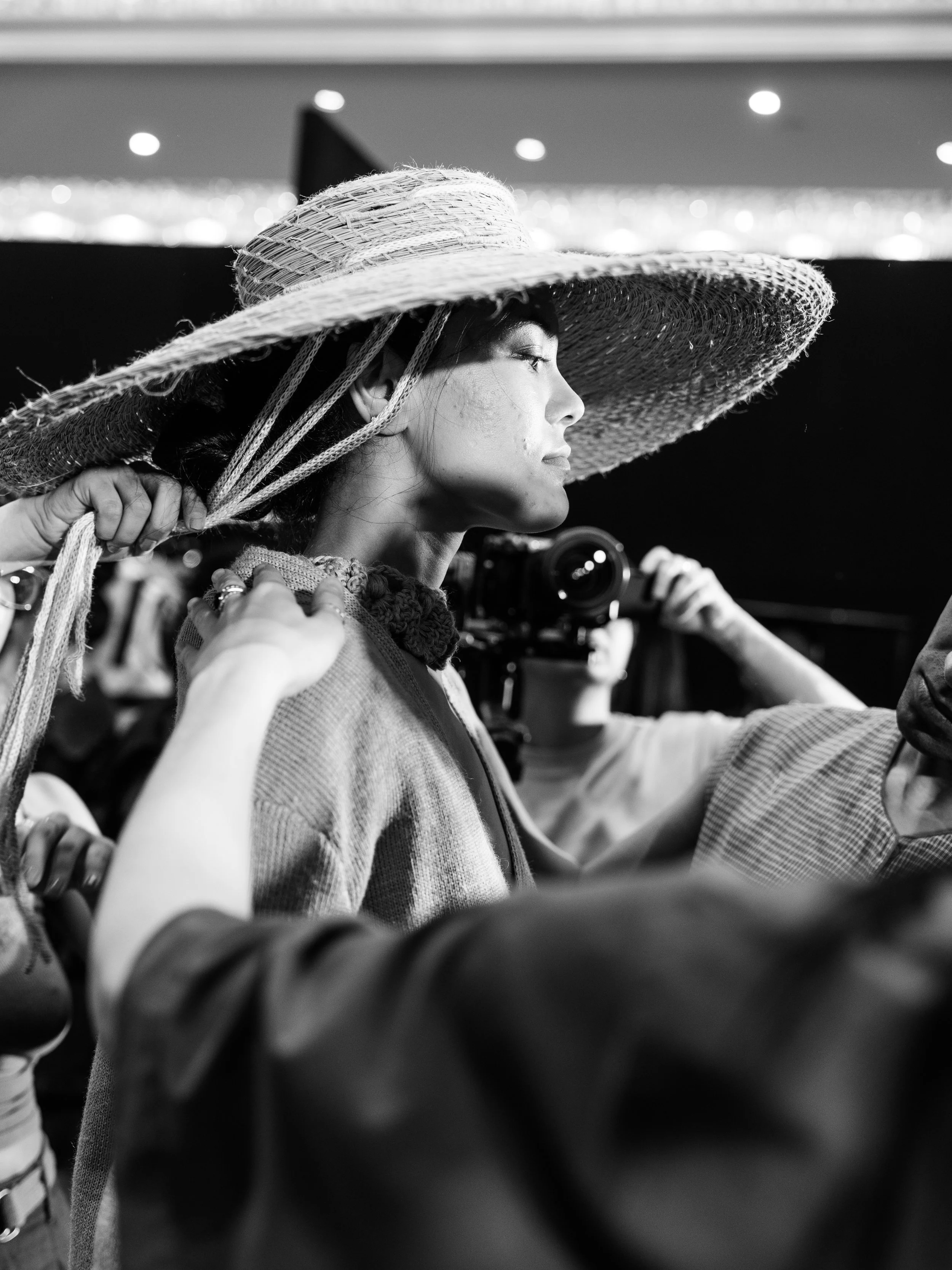 A woman wearing a large woven sun hat, looking to the side, with a focused expression on her face.
