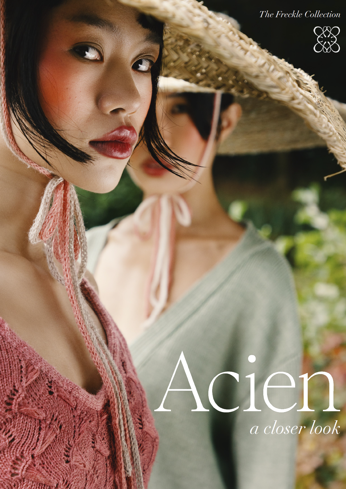 Close-up of two women wearing large straw hats, with one woman in focus and the other slightly blurred in the background, outdoors with greenery.