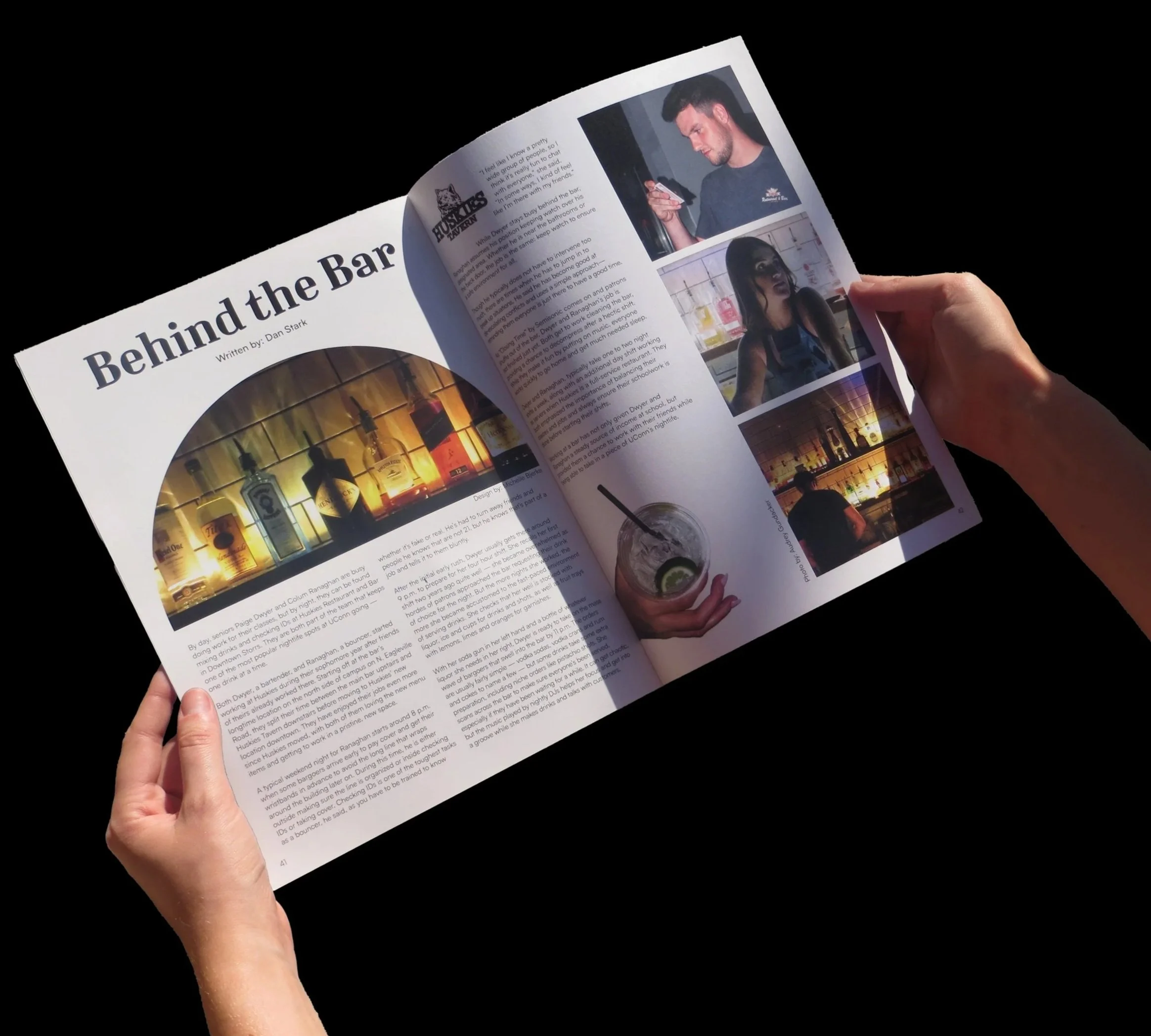Person holding a newspaper or magazine open to an article entitled "Behind the Bar" with photos of a man and a woman at a bar, and a photo of bar bottles and glasses.