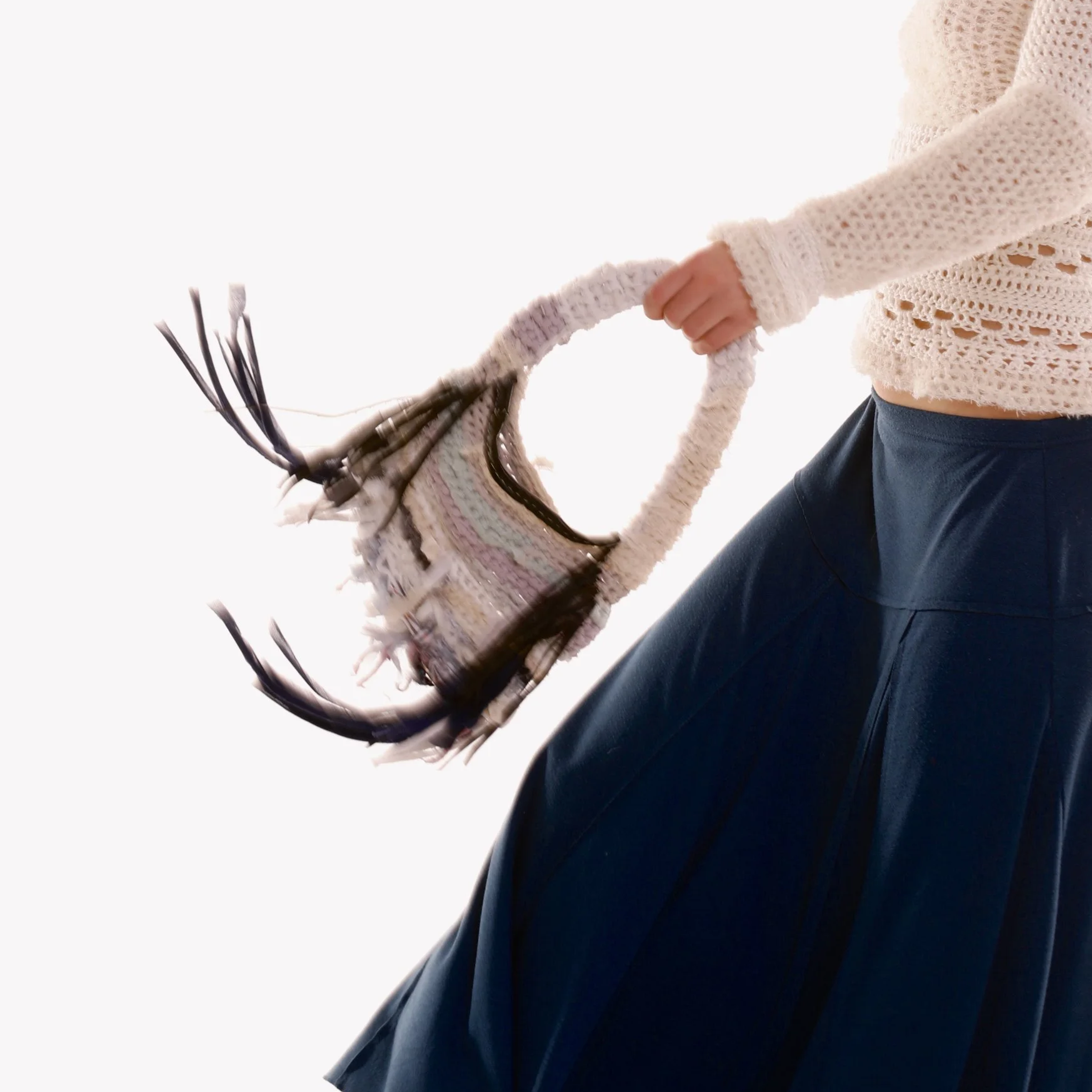 Person wearing a beige knit sweater and dark blue pants holding a blanket with fringes