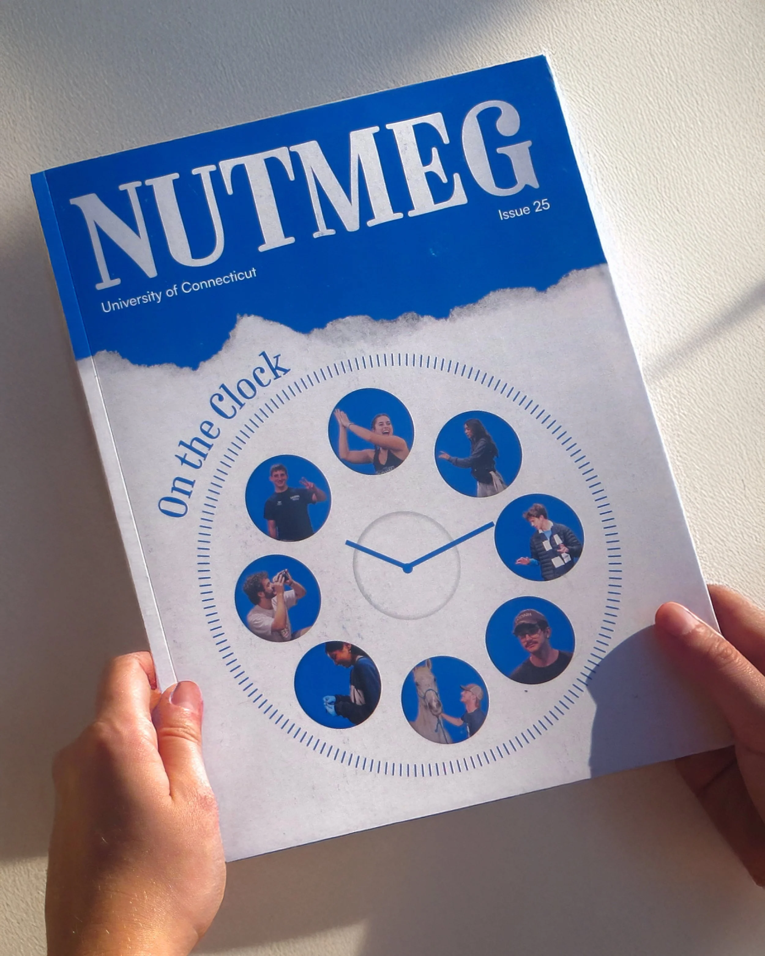A person holding a blue and white calendar or flyer from the University of Connecticut, featuring a clock and pictures of diverse individuals, against a beige background.