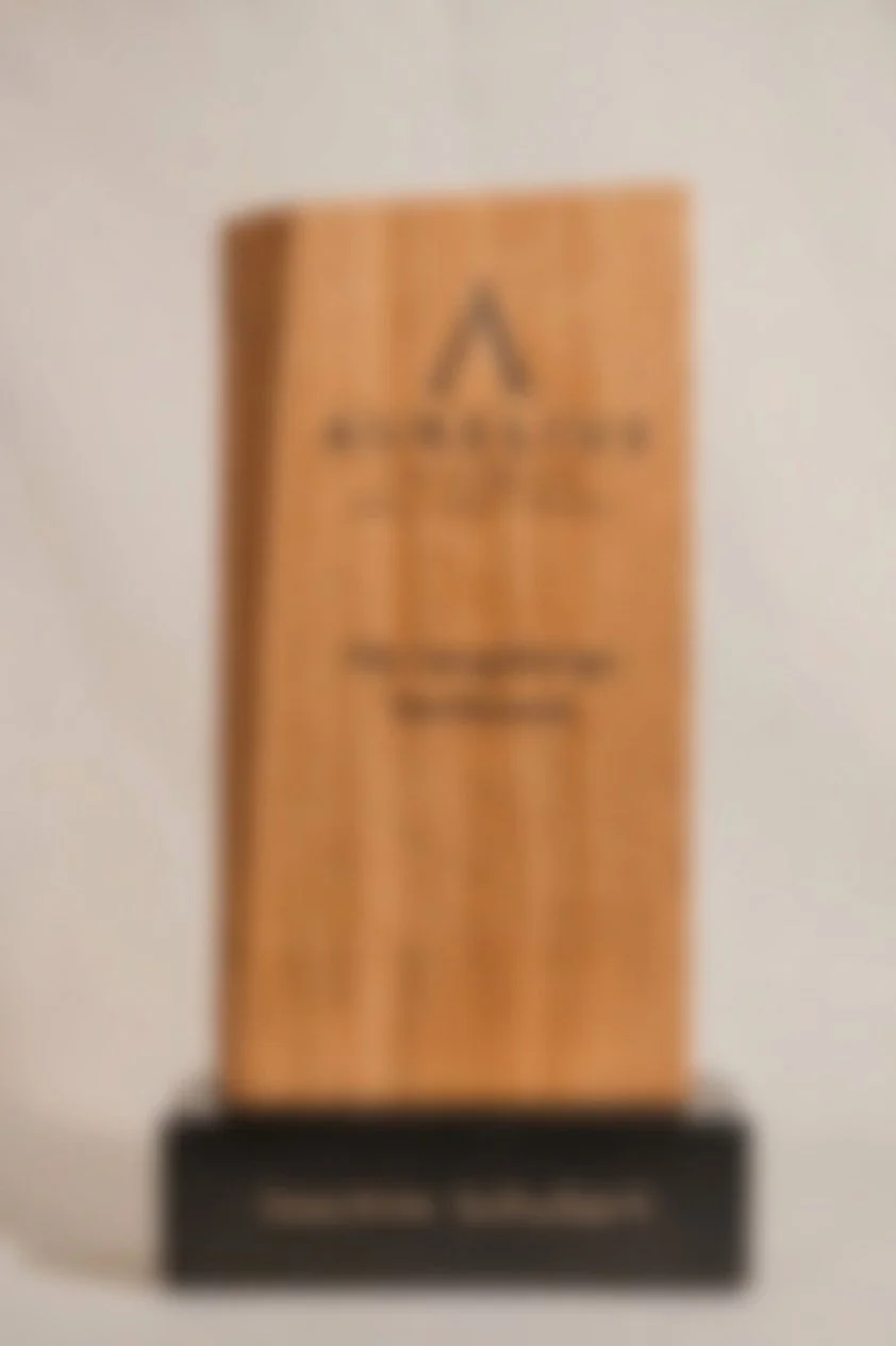 Das Bild zeigt eine aus Holz gefertigte Trophäe mit einer schwarzen Basis, auf der sich eine Glocke befindet.