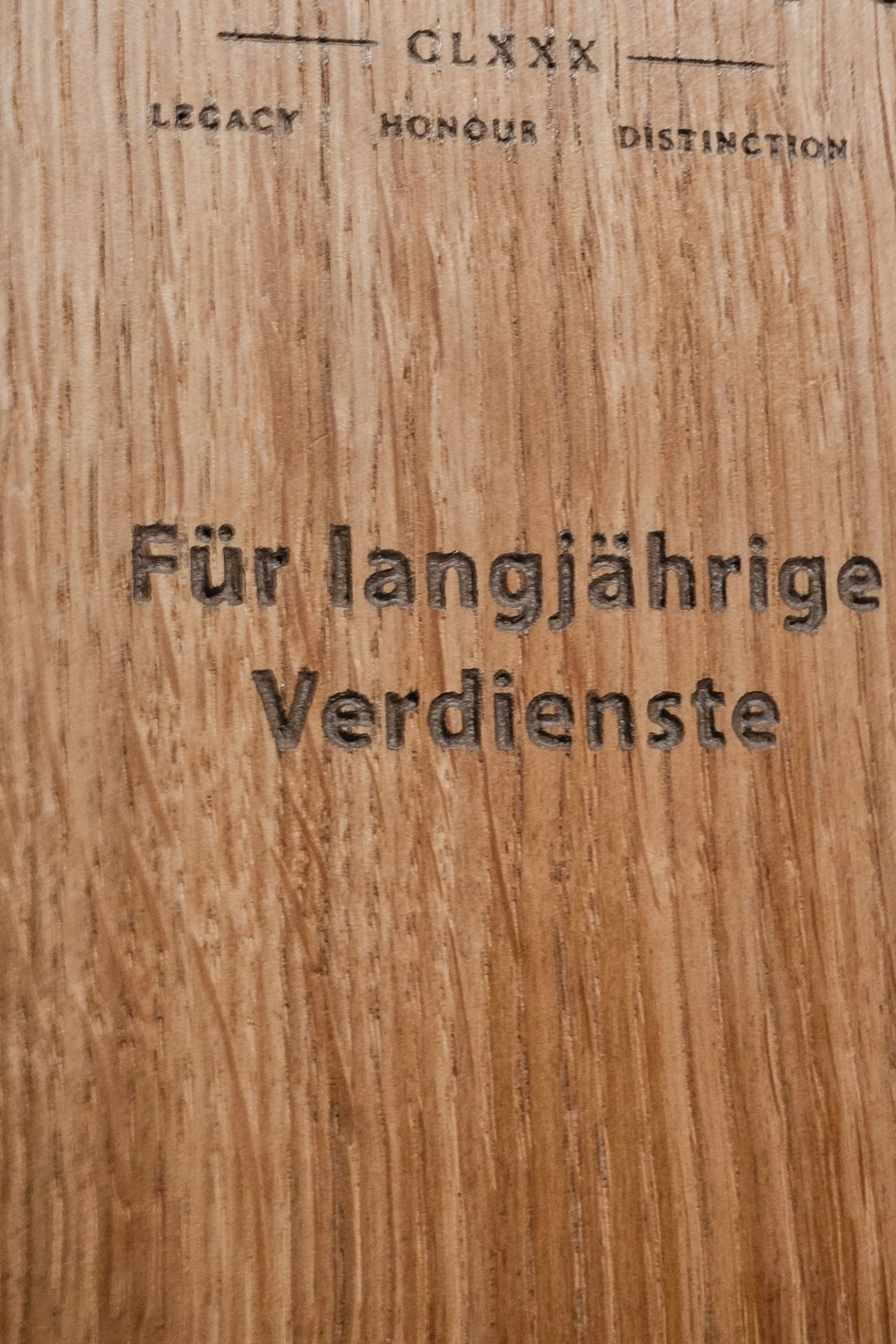 Der Text auf der Holzplatte lautet: 'Für langjährige Verdienste'.