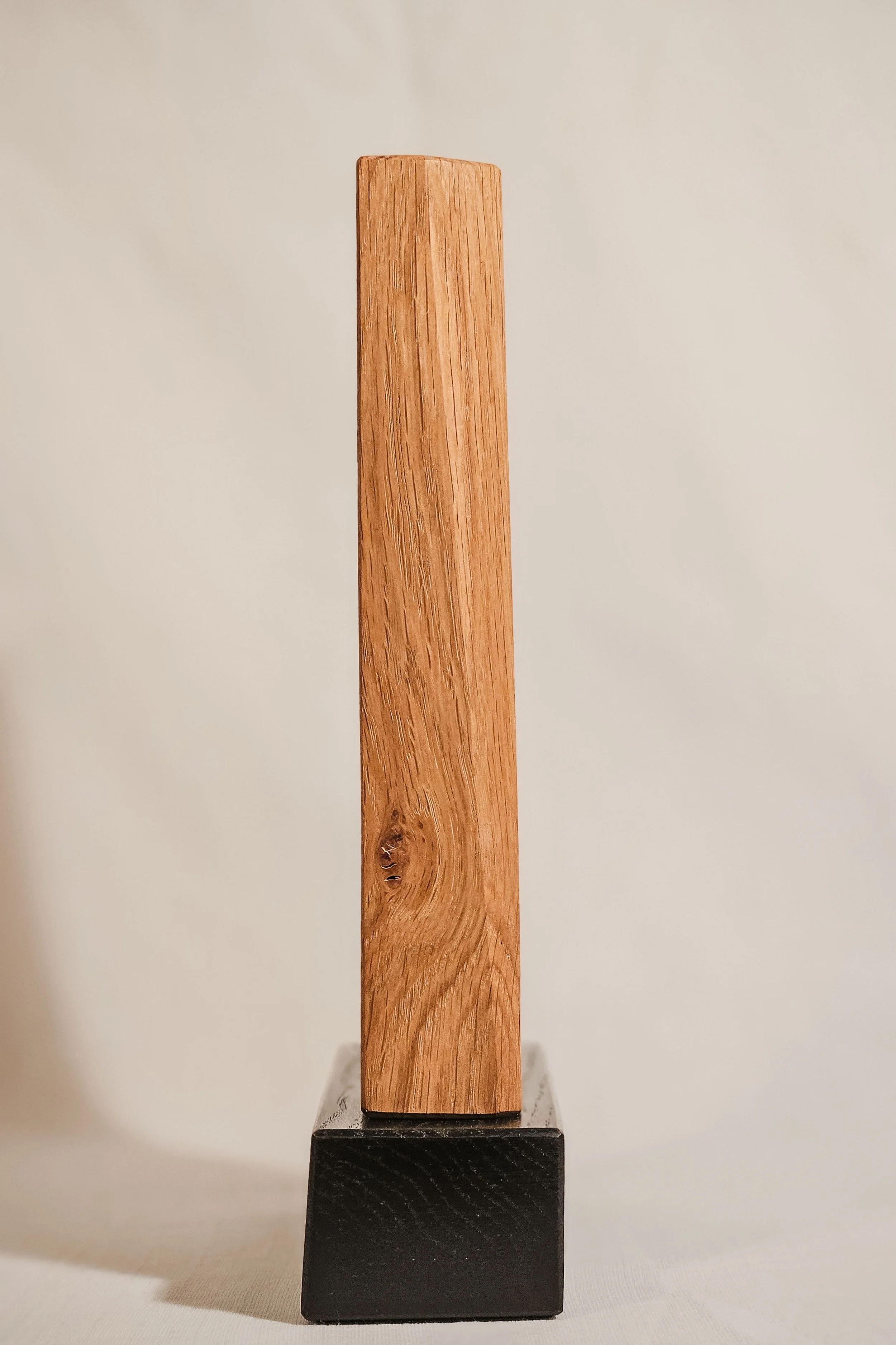 Ein rechteckiges Holzstück auf einem schwarzen Sockel, vor einem weißen Hintergrund.