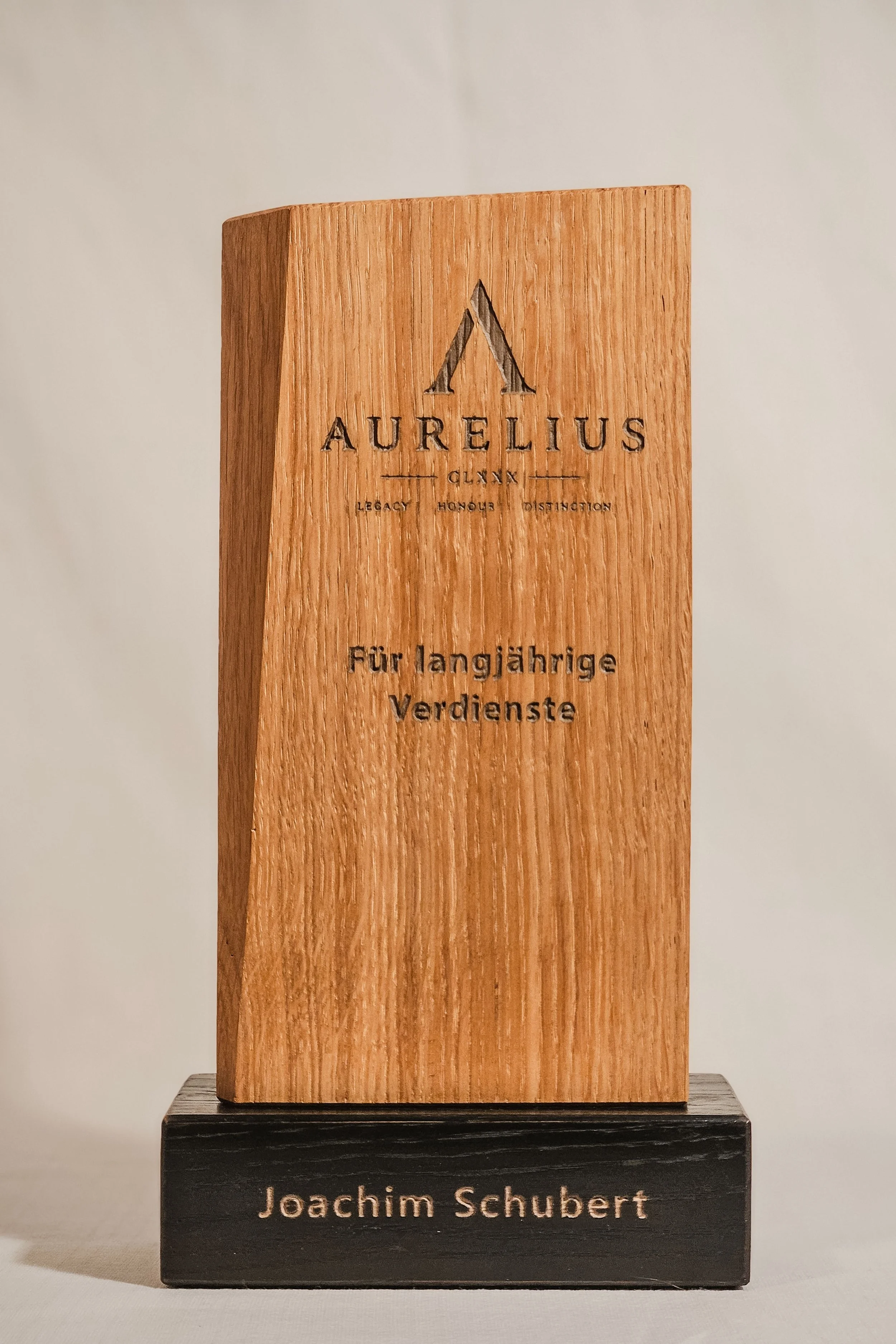 Ein Holzpreis mit dem Namen Joachim Schubert auf einem schwarzen Sockel, auf dem steht Joachim Schubert. Die Holzmarkierung lautet AURELIUS.