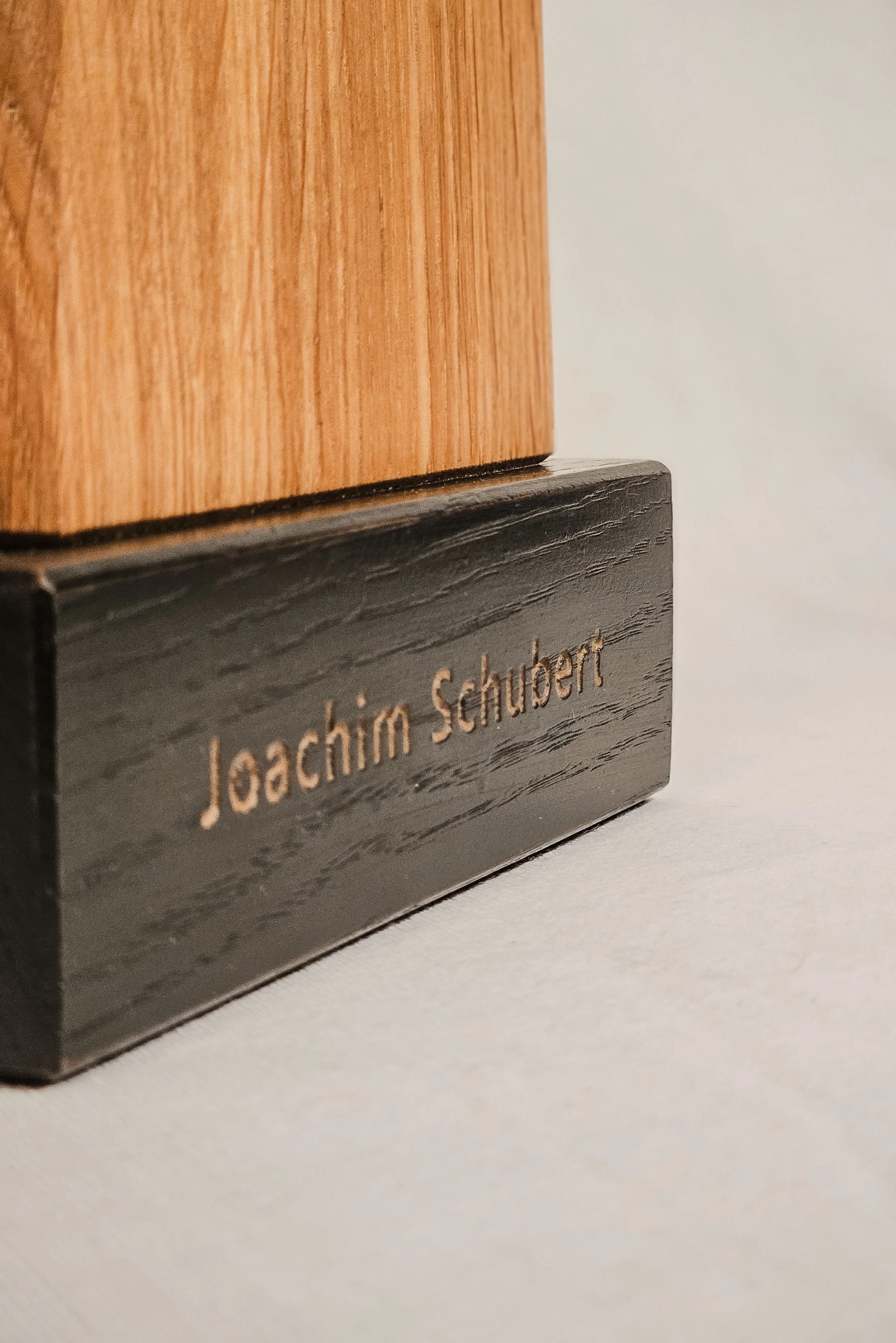 Nahaufnahme eines Holzschilds mit eingravierter Aufschrift 'Joachim Schubert'.
