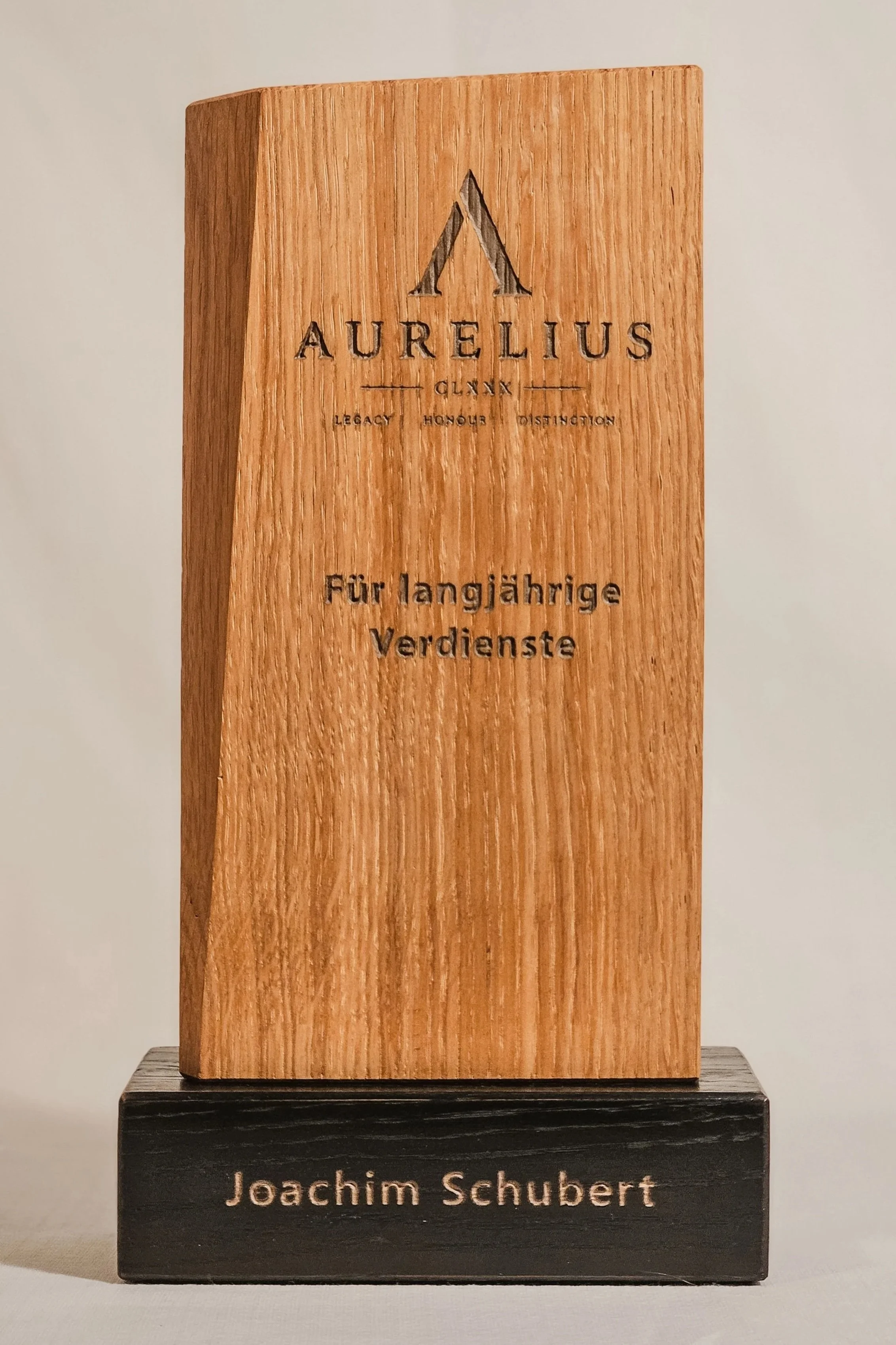Ein Holzpreis in Form eines Holzstücks mit Inschrift "Aurelius" und den Worten "Legacy, Honour, Dedication" sowie einem zweiten Preis aus dunklem Holz mit der Inschrift "Joachim Schubert".
