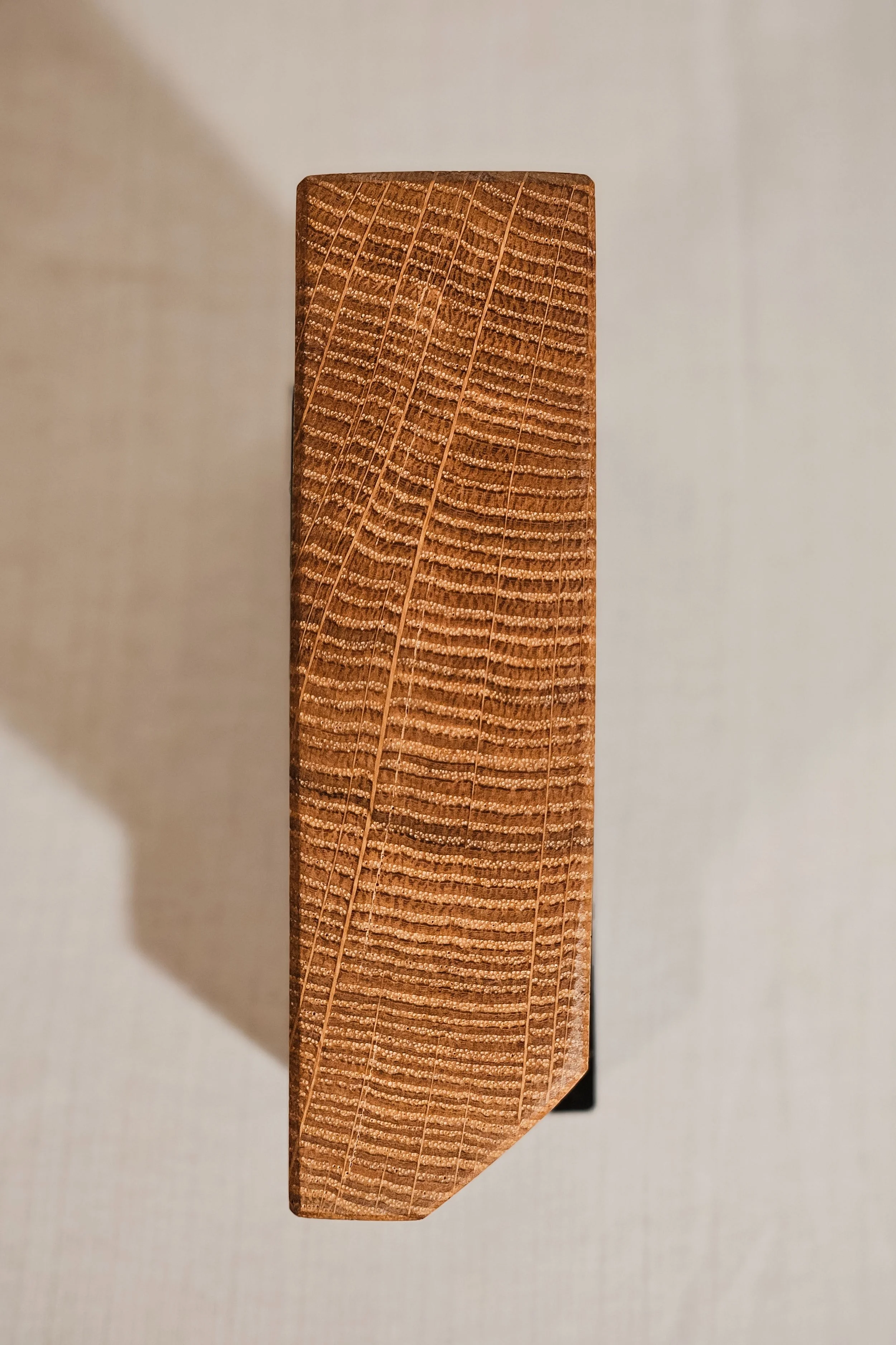 Ein Stück Holz mit gerader Maserung und rechteckigem Querschnitt, auf einer weißen Oberfläche liegend.