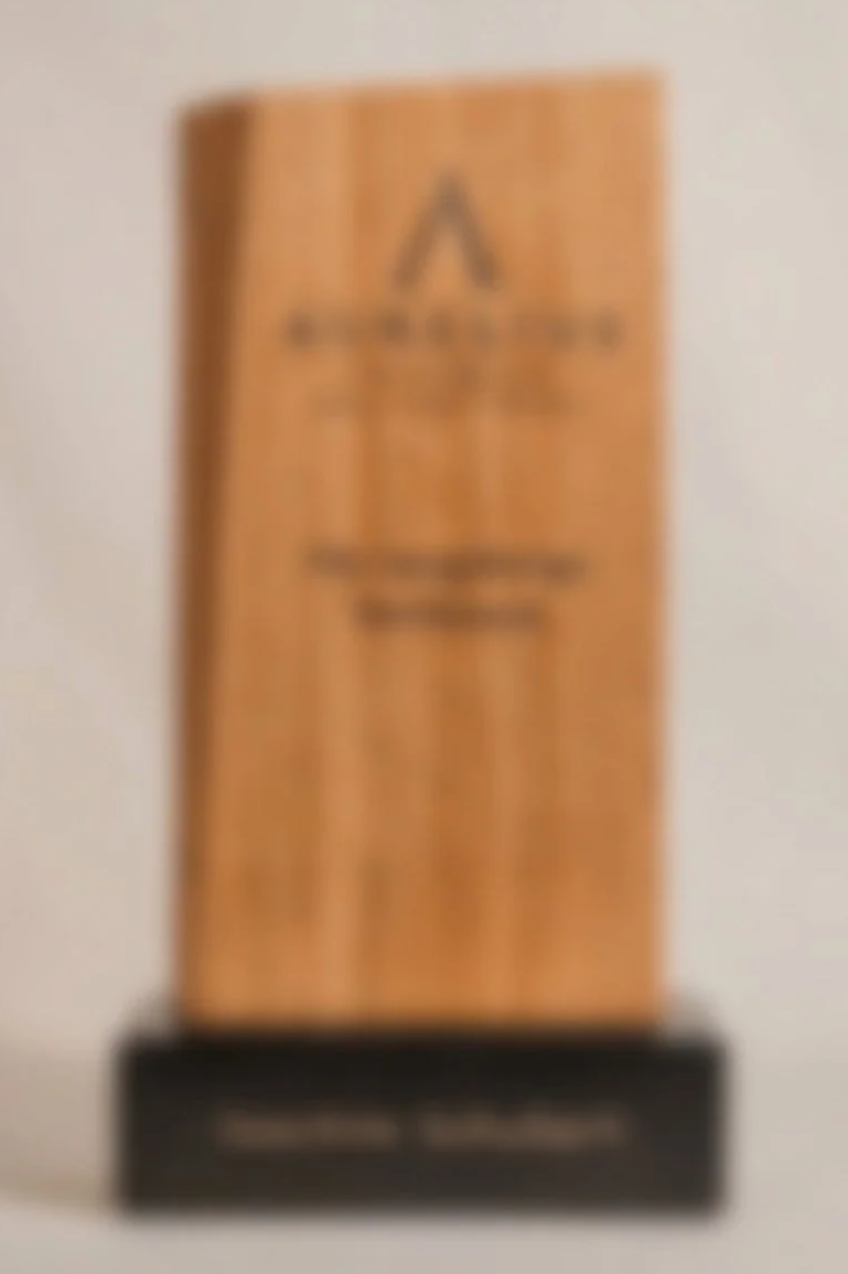 Ein Titel Trophäe oder Auszeichnung aus Holz mit einer eingravierten Marke oder Logo und Text, auf einer dunklen Basise