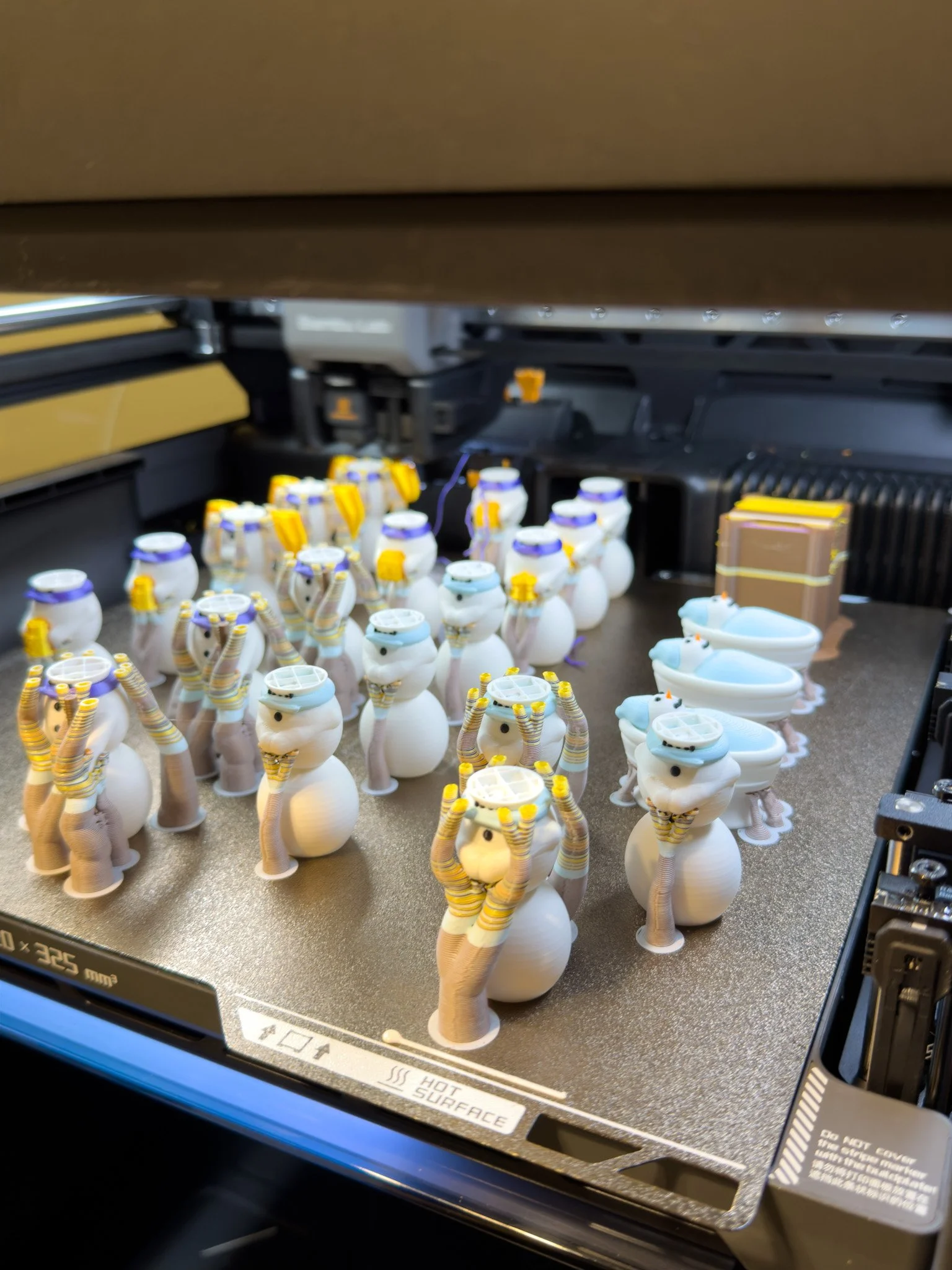 Multiple snowman figures being 3D printed on a multicolor printer bed.