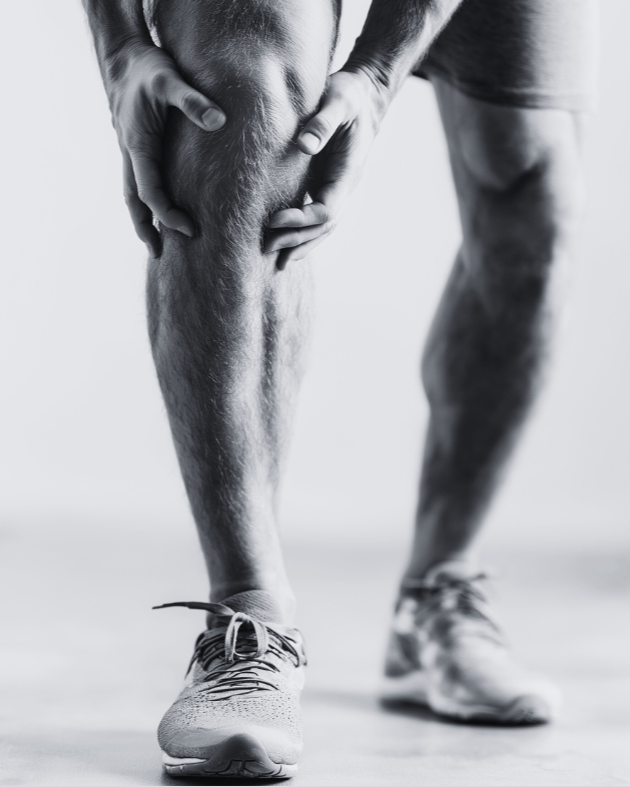 A person holding their knee in pain, standing on a sports court, wearing athletic shoes.