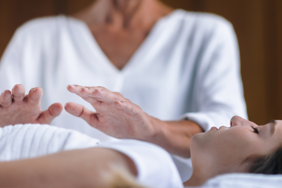 A healthcare professional performing a reiki or healing touch therapy on a patient lying down.