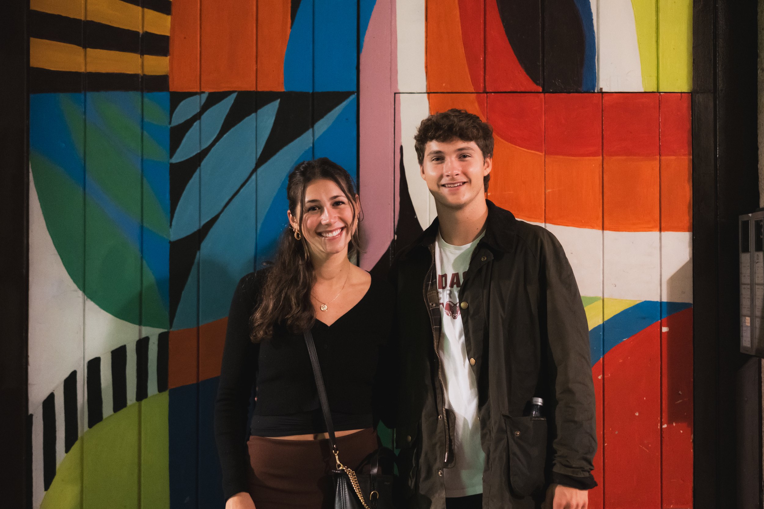 Colorful mural depicting women and children of African descent in traditional clothing on a brick wall, with various smaller graffiti and artwork in the foreground.
