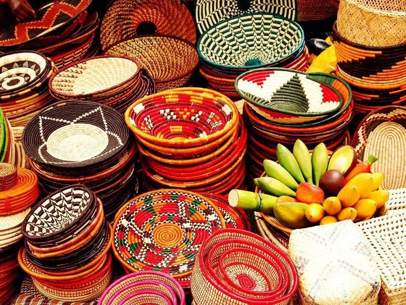 Colorful woven baskets and bowls stacked on a table, with a bunch of bananas and other fruits in front.