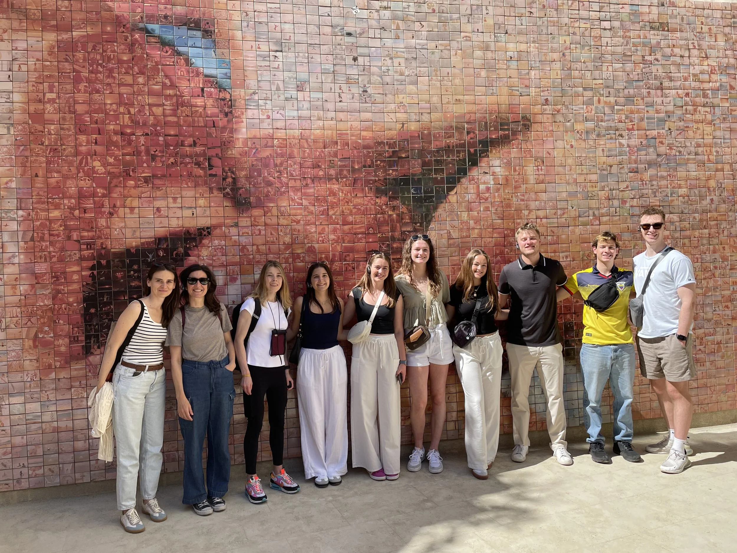 People walking along a narrow, cobblestone street between old stone buildings with decorative architectural elements and bridges.