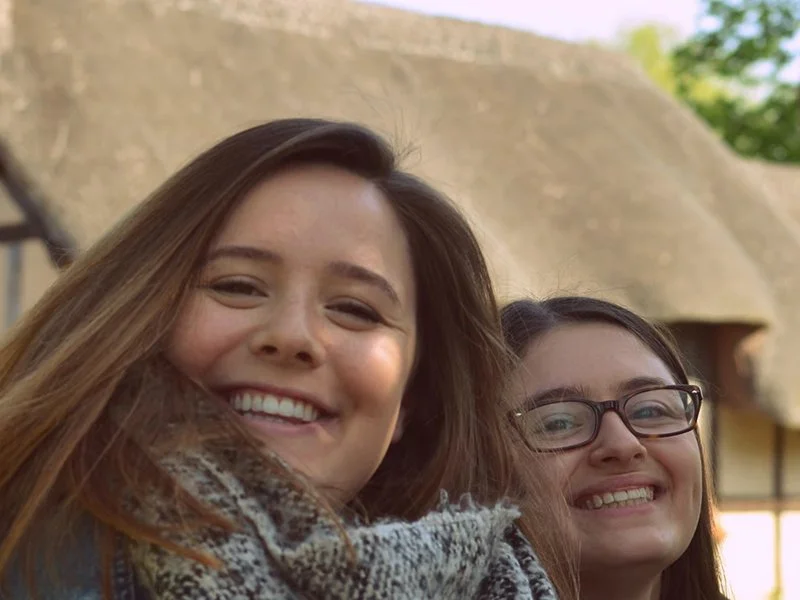 Two young women smiling outdoors with a large stone structure in the background.