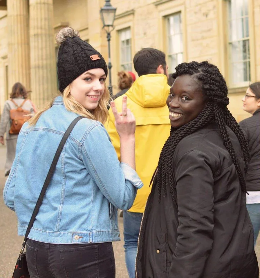 People walking and standing on grassy cliffs overlooking a coastline with white chalk cliffs and green fields in the background.