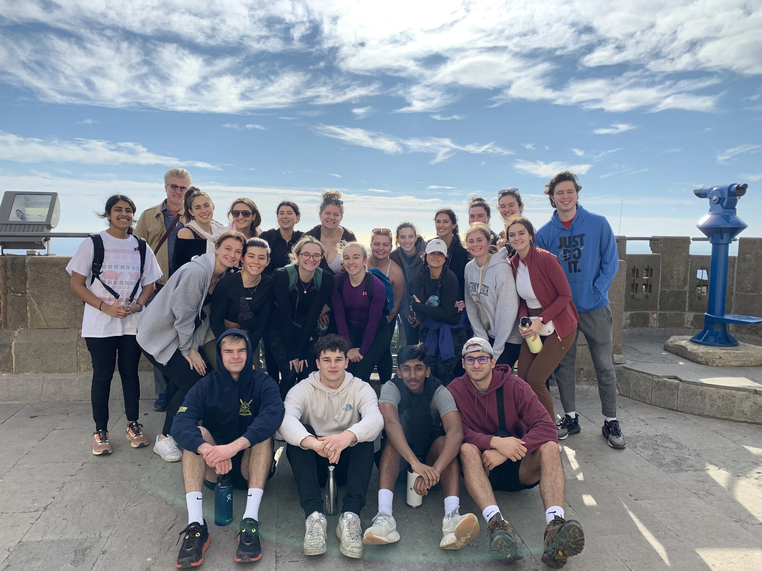 The Griffith Observatory on a hill with lush green trees, overlooking the city of Los Angeles with tall buildings and a clear blue sky.