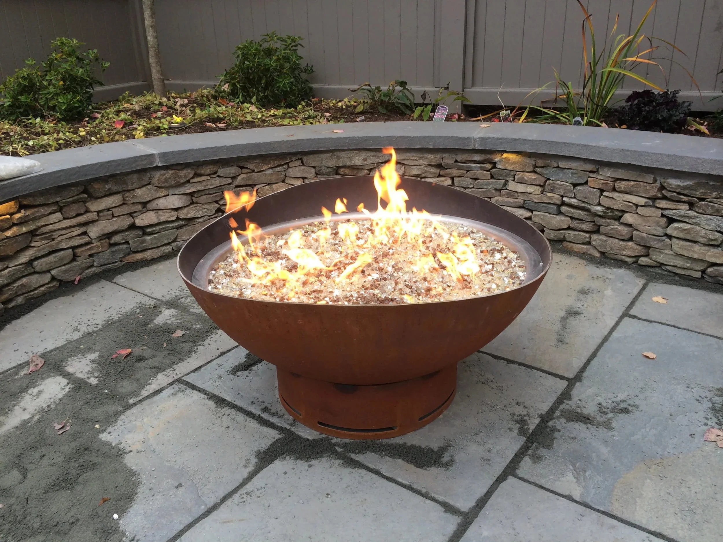 A contemporary fire pit installed within a paver patio as part of landscape construction in North Kingstown, RI
