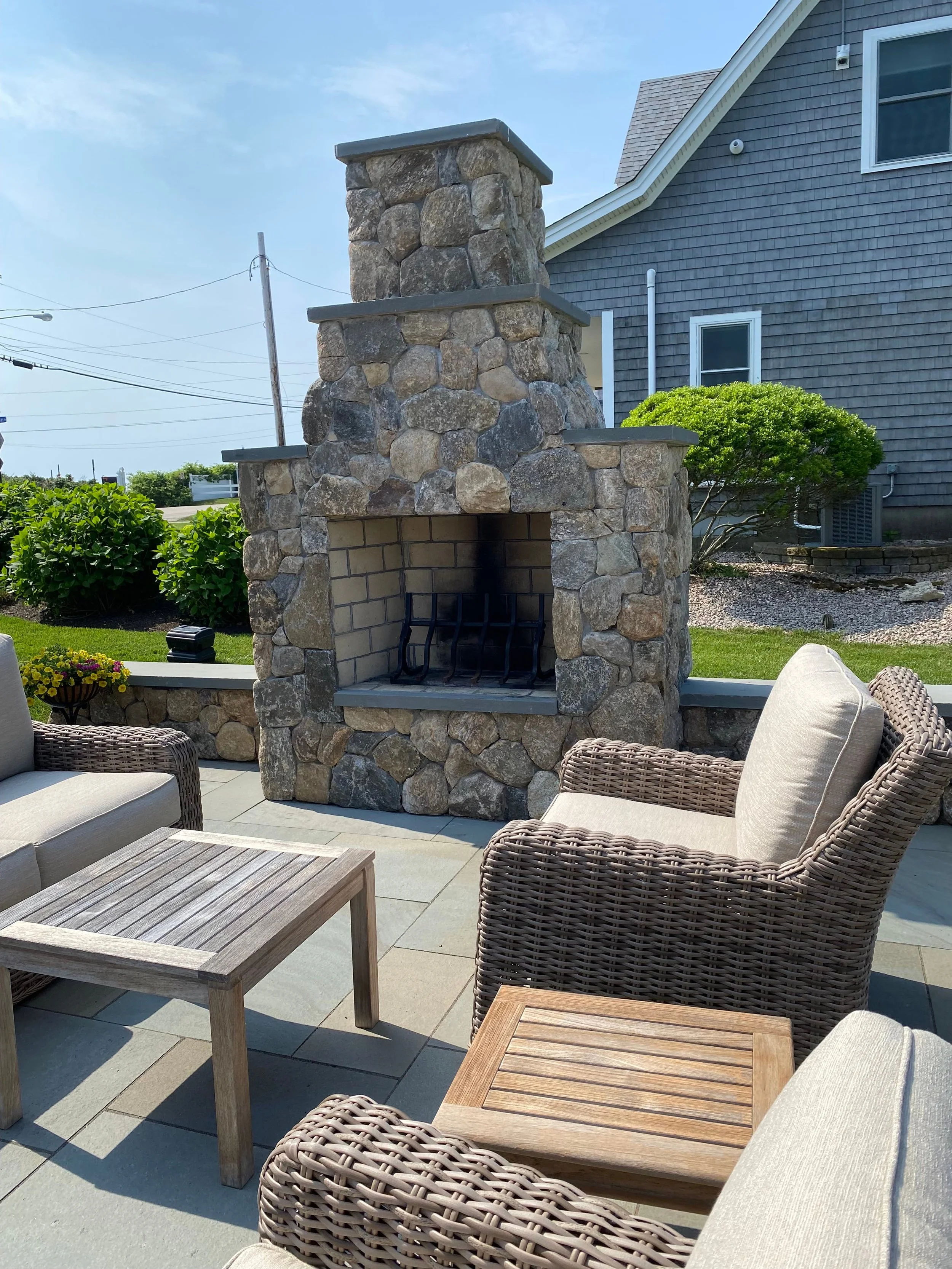 A custom outdoor fireplace built with natural stone on a paver patio seating area in Westerly, RI